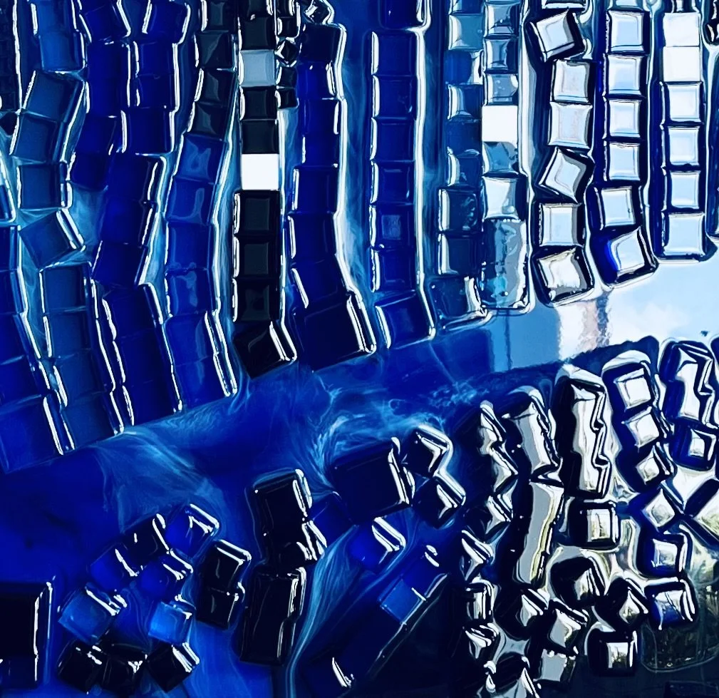 Close-up of a metallic abstract artwork with square and rectangular tiles in shades of blue, black, and white.