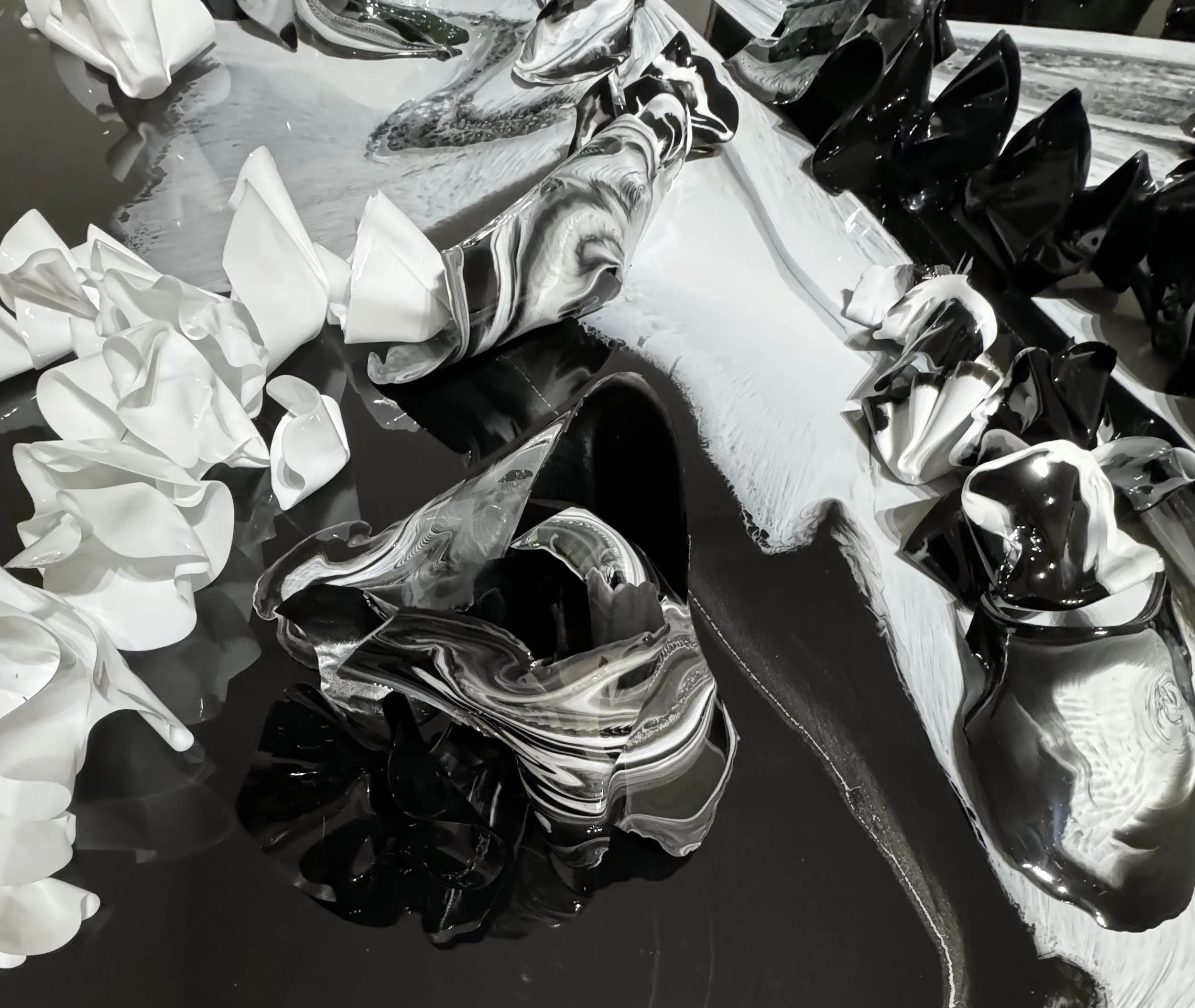 Close-up of black, white, and marbled acrylic paint sculptures or mixed media art with irregular shapes and textures, featuring ruffled, glossy, and smooth surfaces.