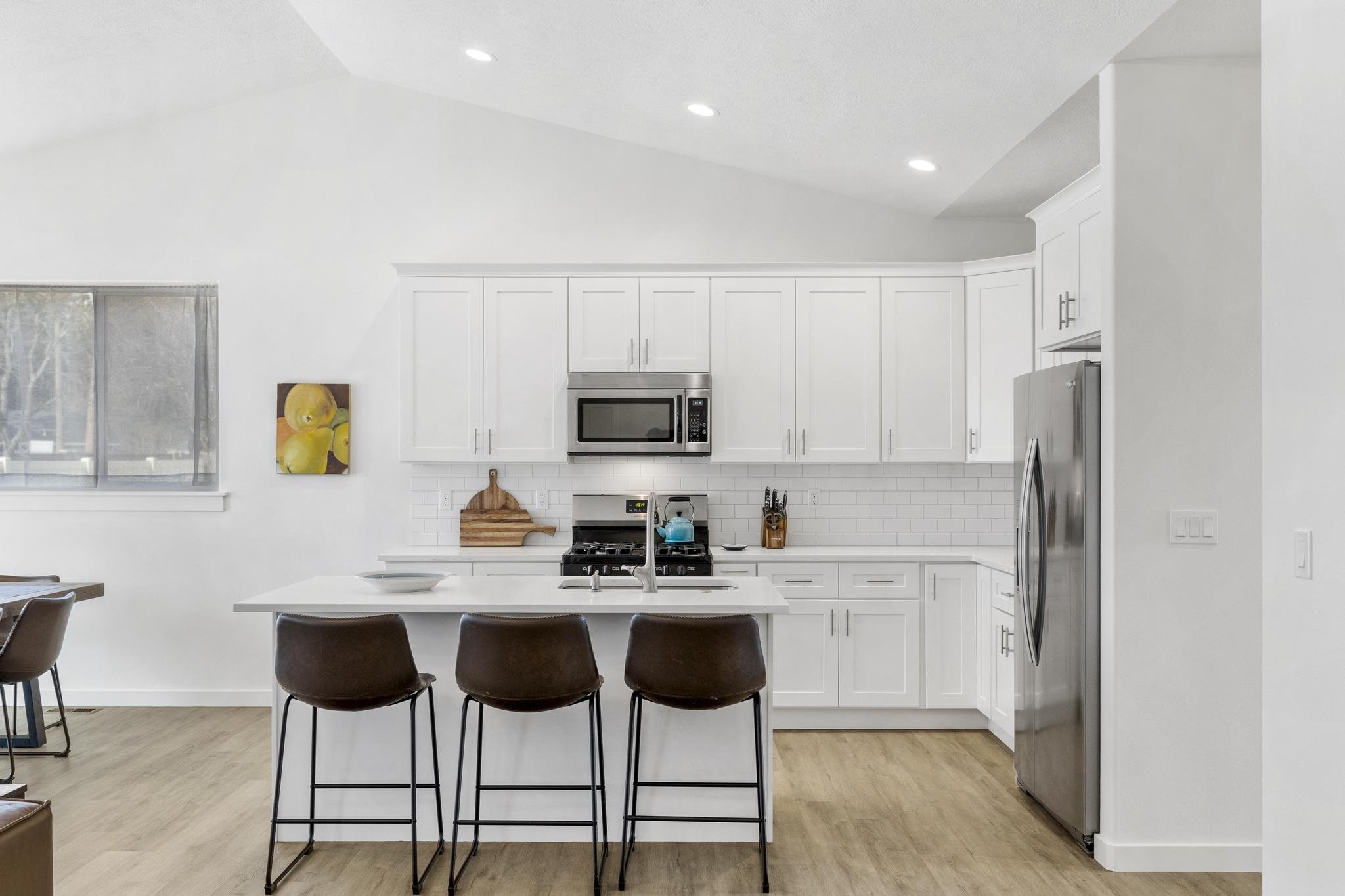 Modern kitchen with white cabinets, stainless steel appliances, and island with three brown chairs.