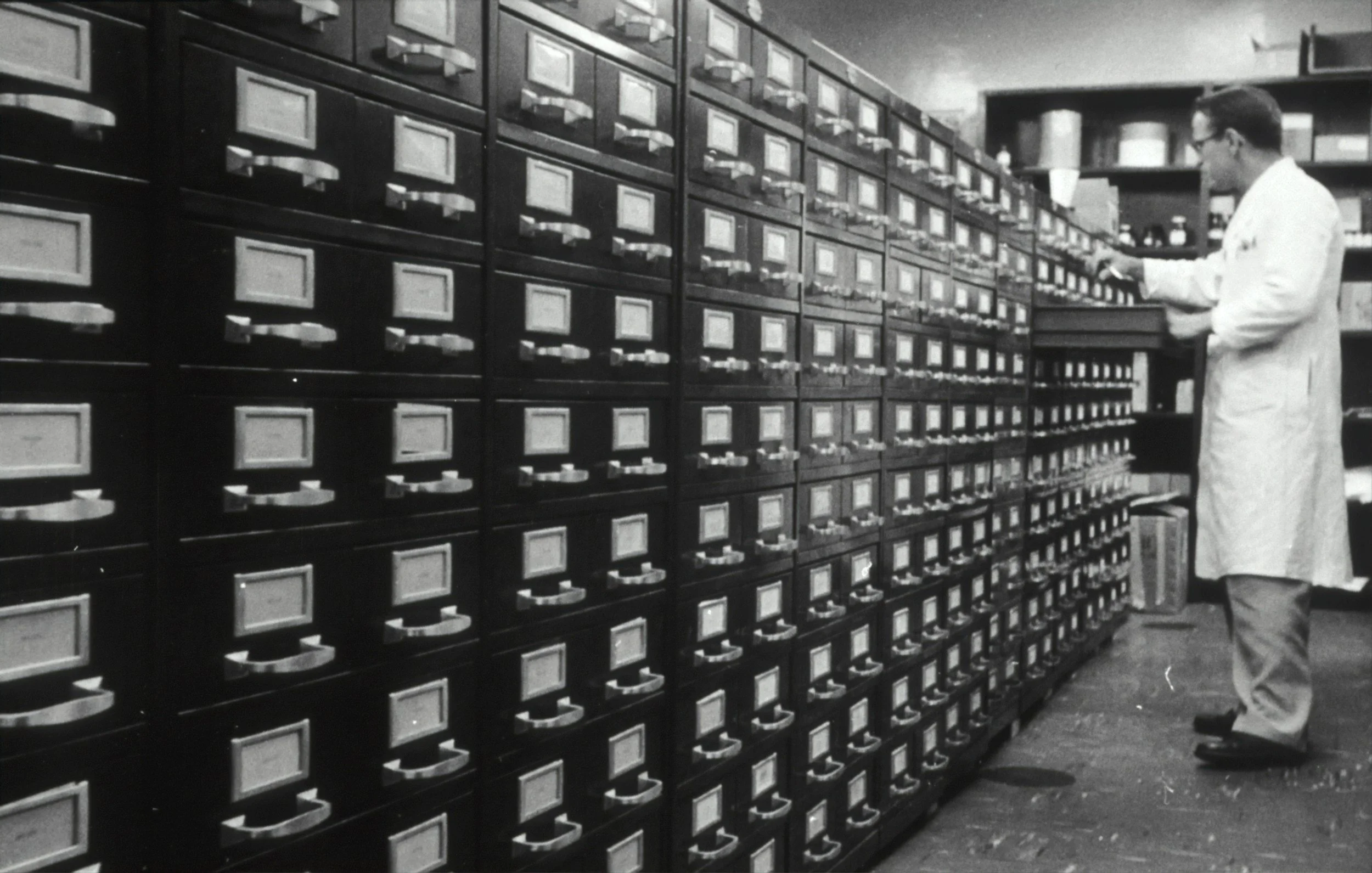 A man in a lab coat working with rows of filing cabinets in a storage room.