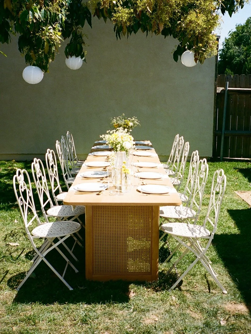 Outdoor backyard table setup with cane-leg dining table and white vintage bistro chairs arranged for an intimate gathering
