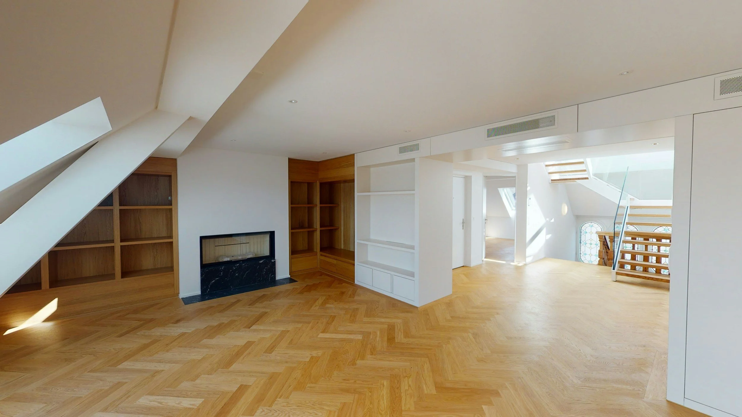 Bright, spacious living room with I-shaped wooden flooring, built-in white shelving, a black marble fireplace, built-in wooden shelves, and natural light from large skylights and windows.