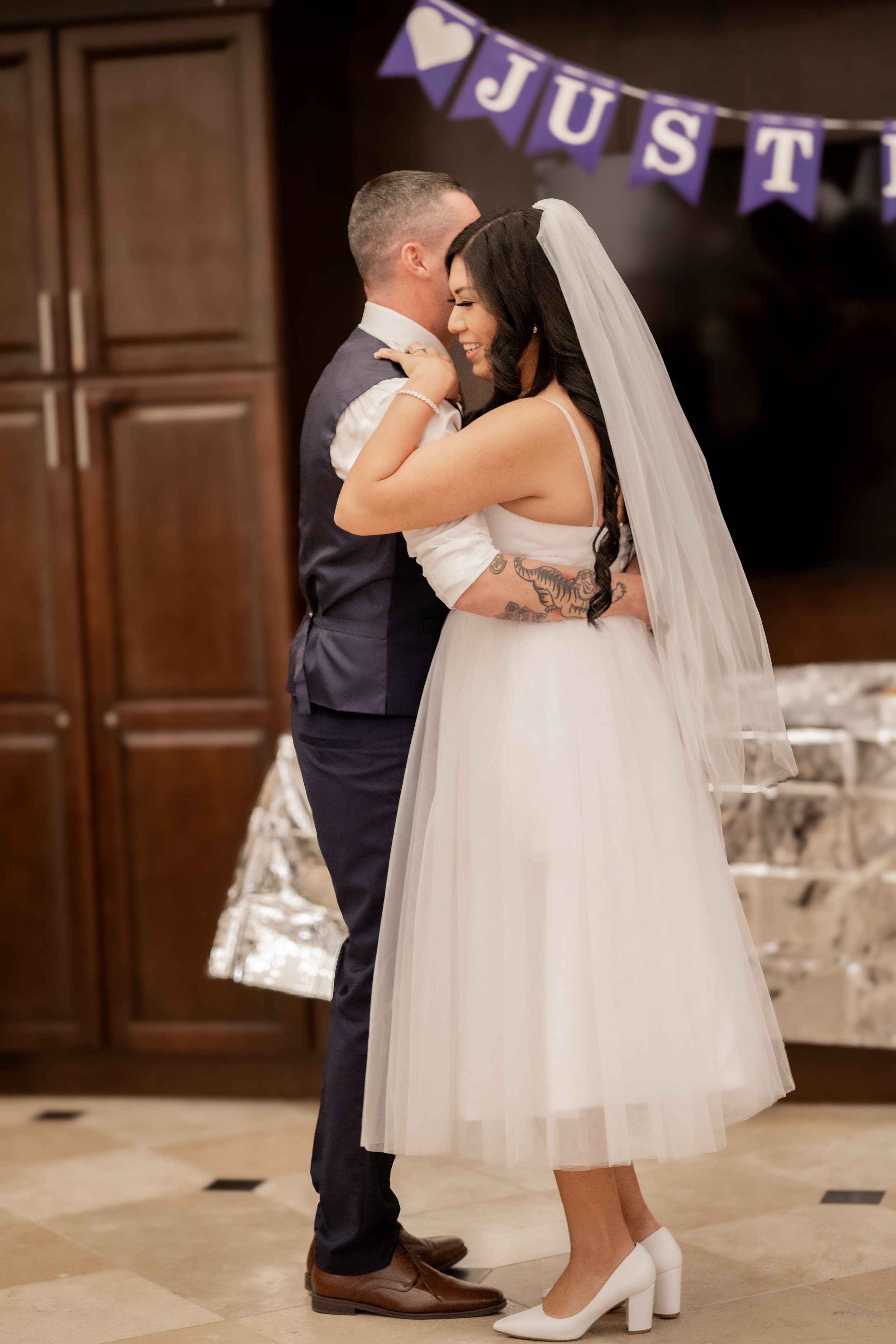 A bride and groom share a dance at their wedding reception, with a purple banner spelling "JUST" in the background.