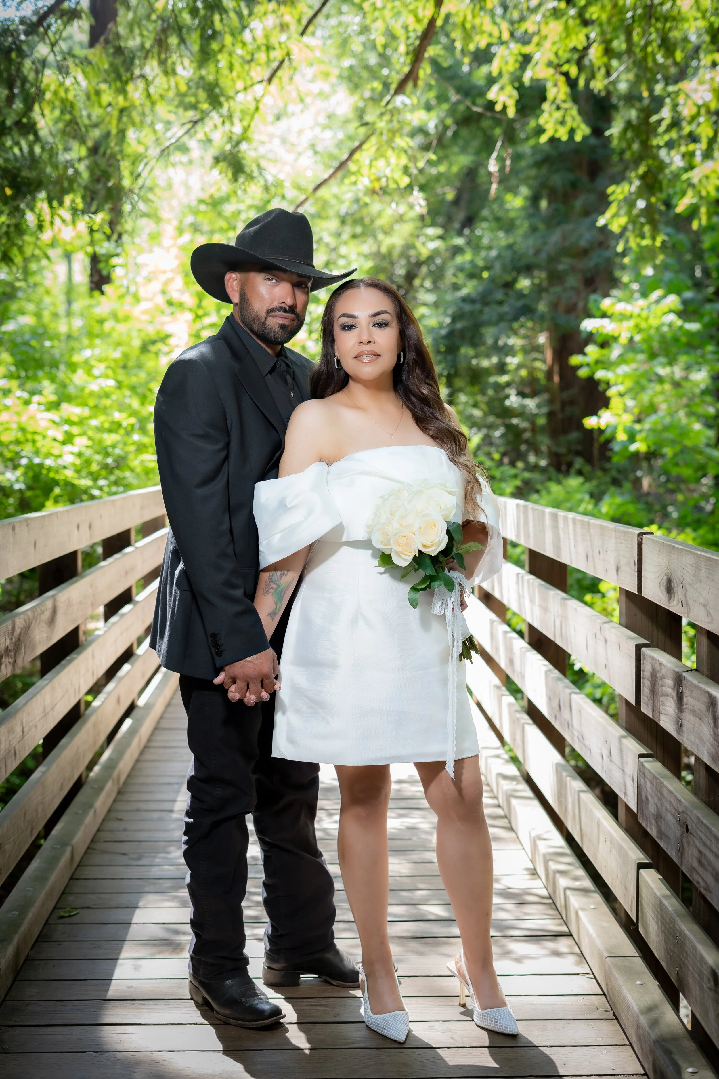 an engaged couple standing on a bridge, holding hands with a green scenery