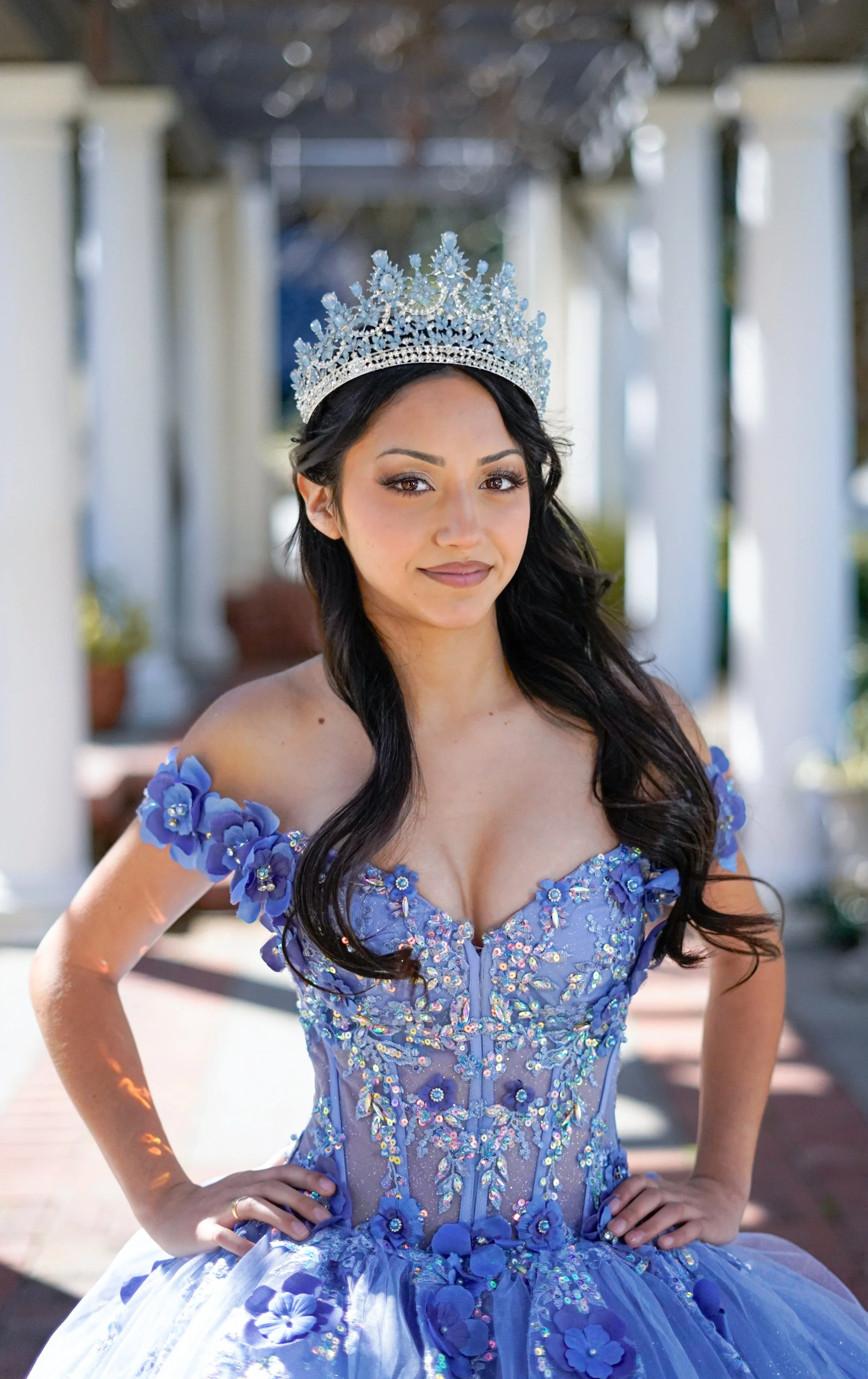 a young girl in a blue dress with a crown posing in a walk way
