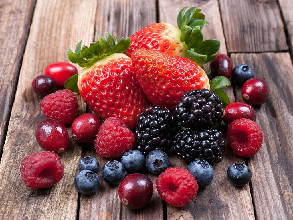 Assorted fresh berries on wooden surface, including strawberries, blackberries, raspberries, blueberries, and cranberries.