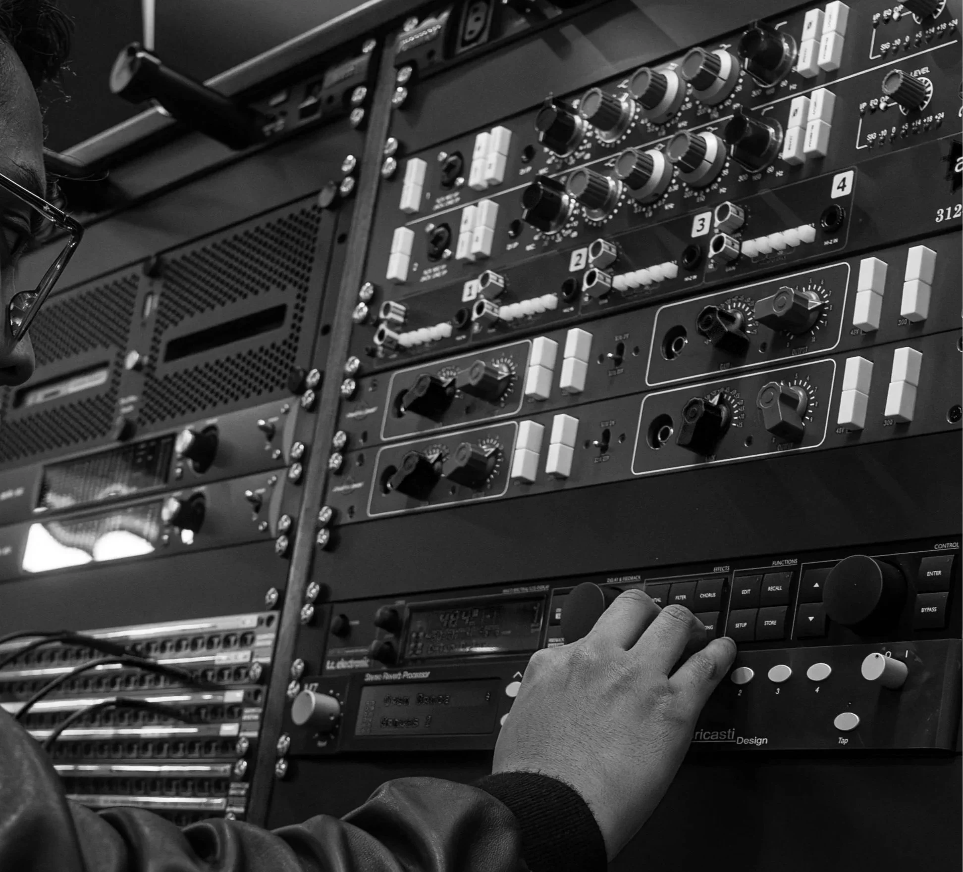 A person adjusting settings on an audio mixer with multiple dials and controls in black and white.
