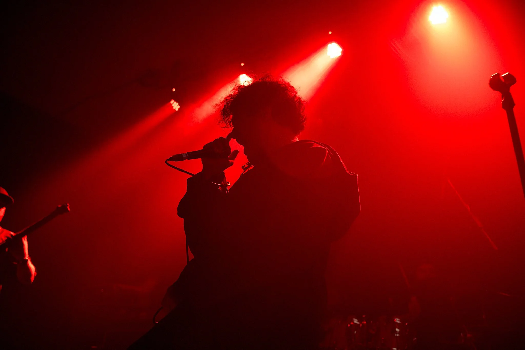 Silhouette of a singer holding a microphone on stage with red lights shining behind him.