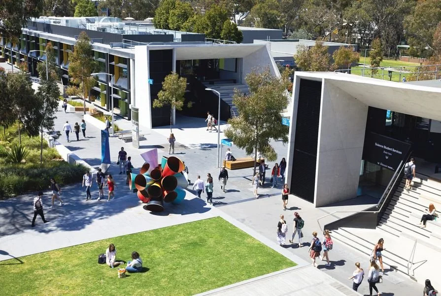 An educational building with a grand entry stair and students sitting or on foot at Monash University Clayton