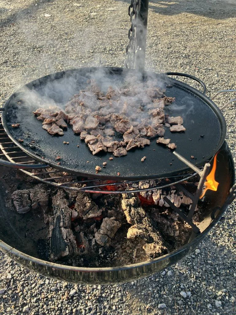 Kjøtt som stekes på en utendørs grillplate over åpen ild.