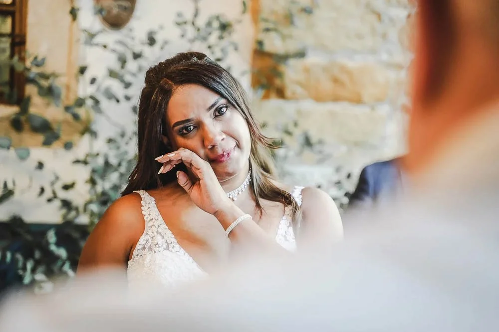 Eine Frau in einem weißen Hochzeitskleid, die emotional ist und Tränen der Freude oder Rührung in den Augen hat, während sie mit einem Mann spricht.