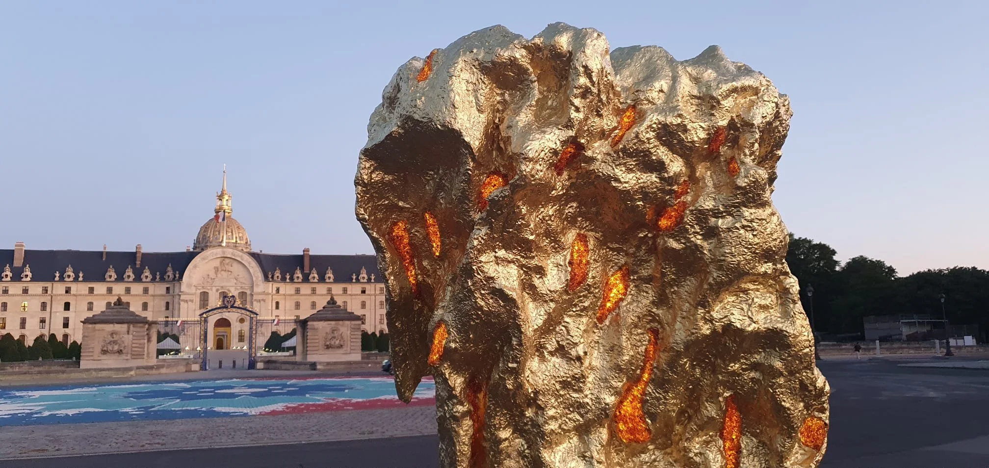 Large abstract bronze sculpture made of textured gold, baltic amber and solid gold, located Place des invalides in Paris. In the background and a clear evening sky.