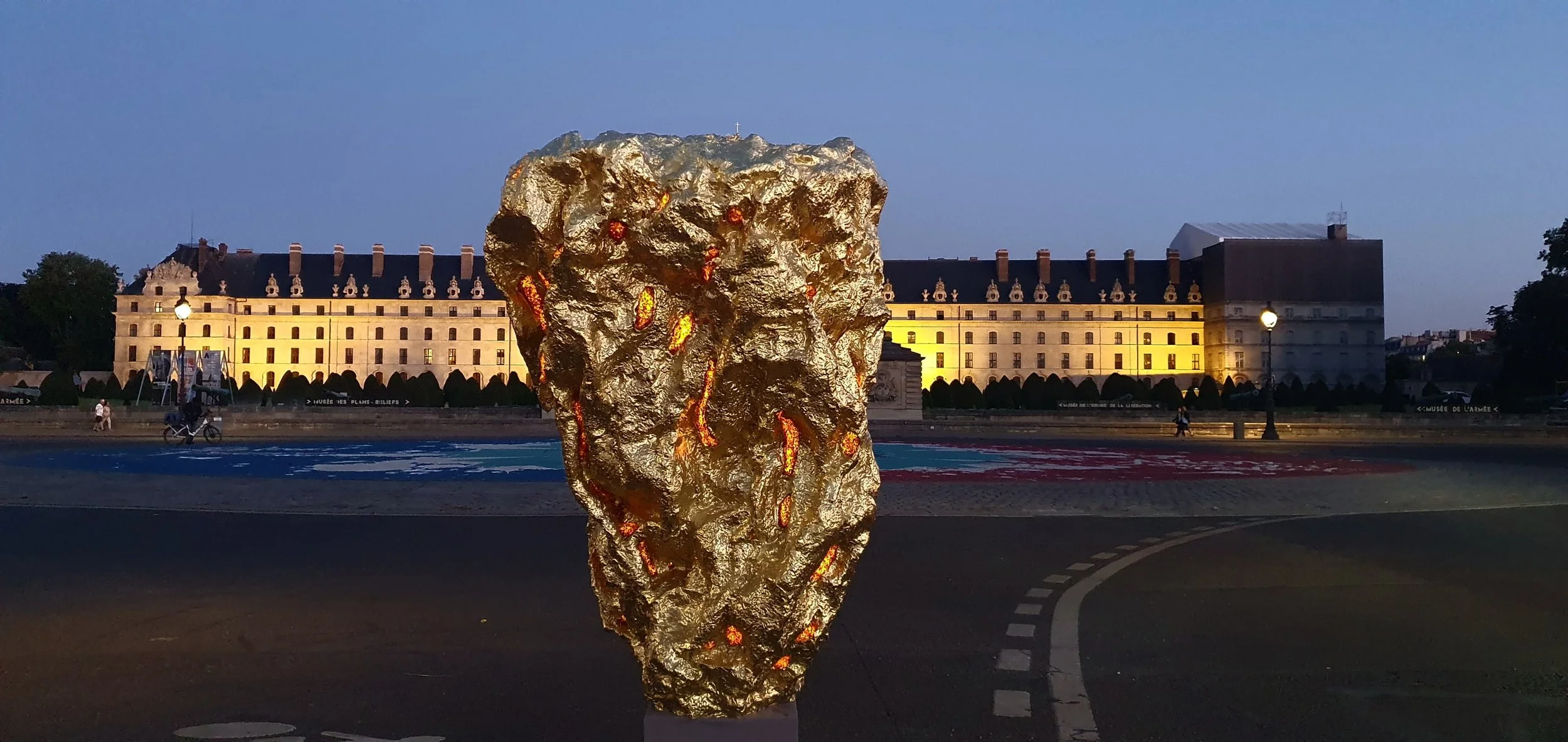 Large abstract bronze sculpture made of textured gold, baltic amber and solid gold, located Place des invalides in Paris. In the background and a clear evening sky.