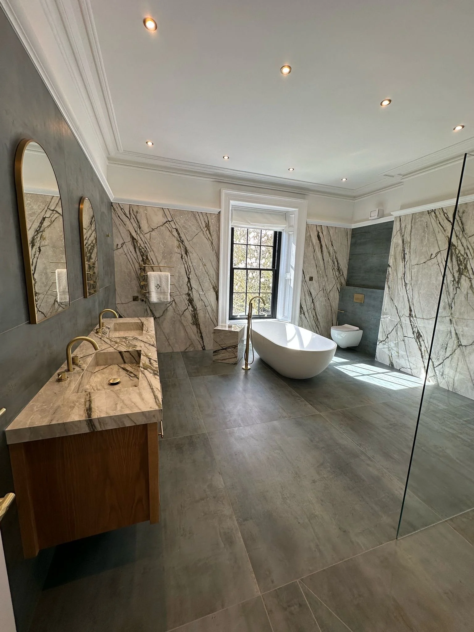 Large family bathroom. Double shower. Large format tiles. Recessed shelves. Mitred edges. Double vanity. Bespoke double basins. Illuminated mirrors. Free standing bath. Floor mounted bath tap.