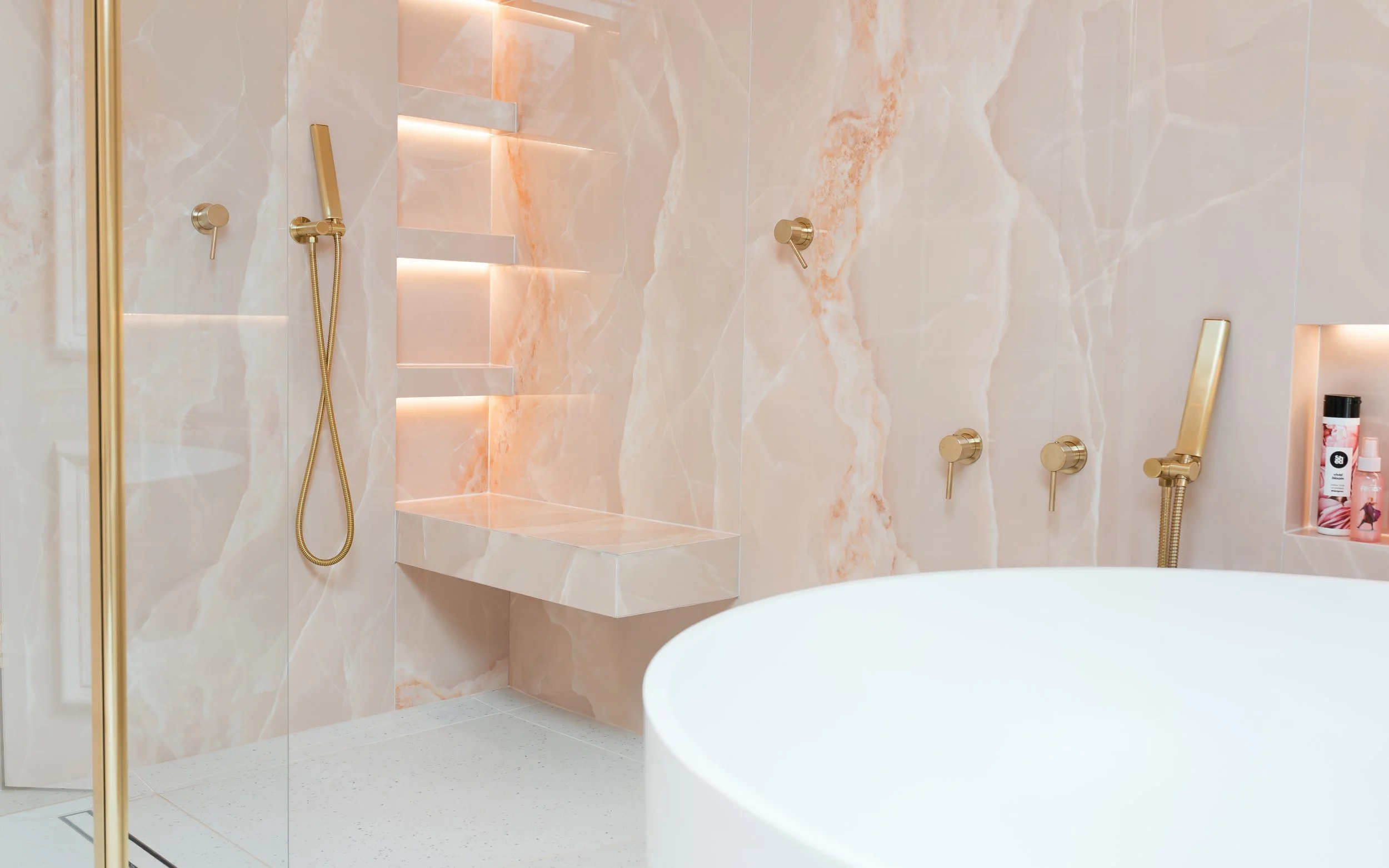 Pink onyx en-suite. Large format tiles. Flowing recessed shelves. Mitred edges. Bespoke vanity.