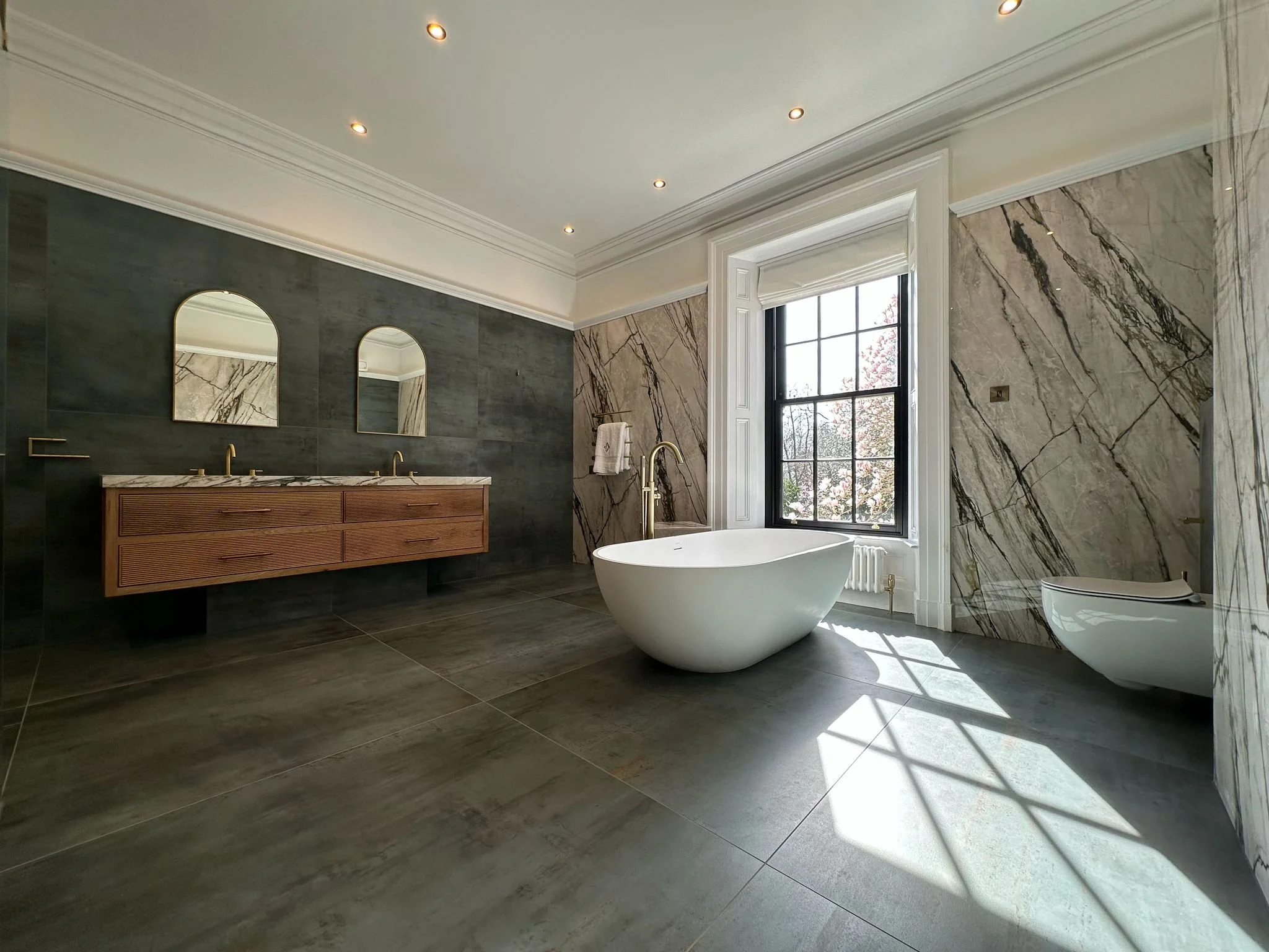 Large family bathroom. Double shower. Large format tiles. Recessed shelves. Mitred edges. Double vanity. Bespoke double basins. Illuminated mirrors. Free standing bath. Floor mounted bath tap.