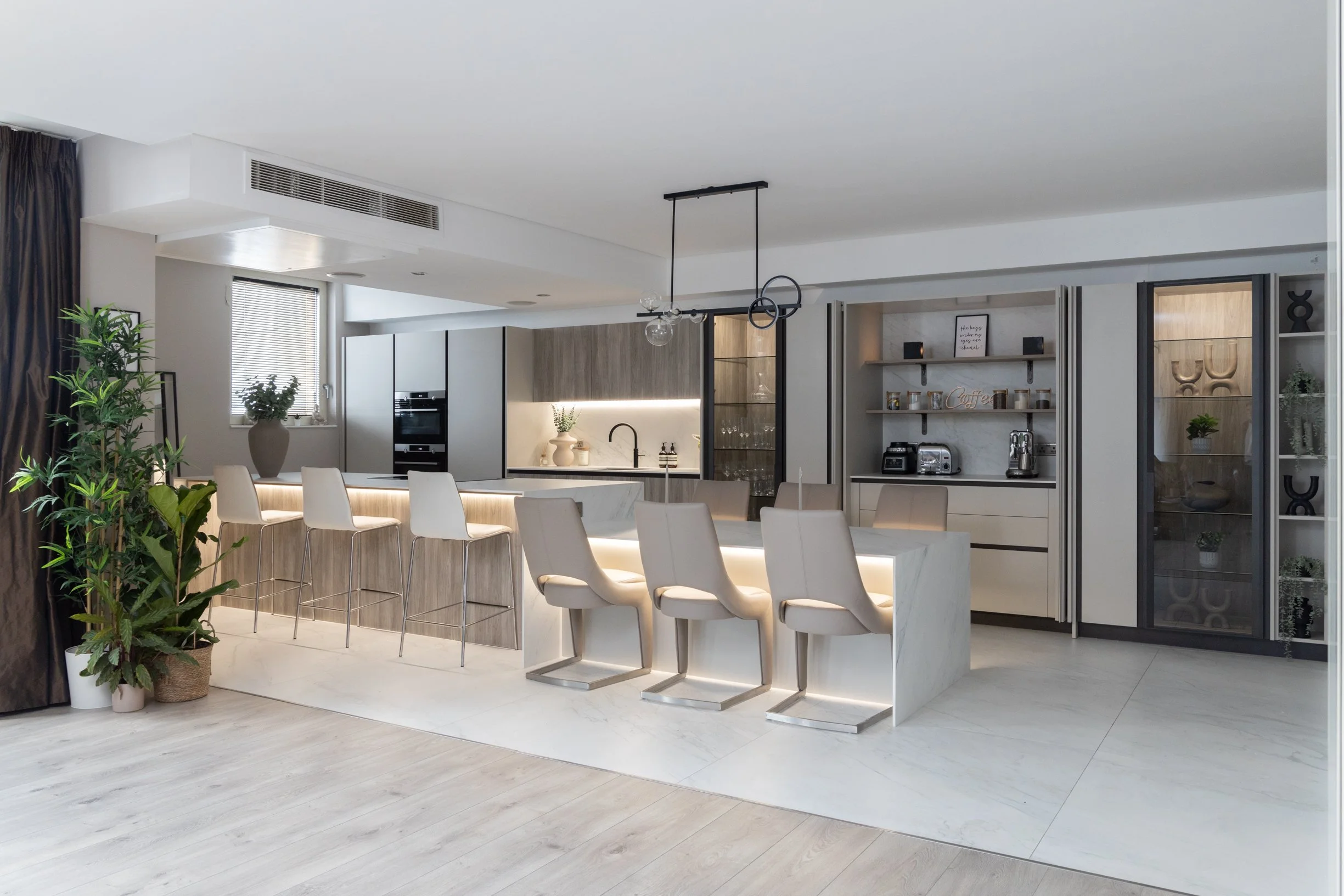 Penthouse apartment kitchen. Oversized, split level kitchen island. Breakfast station with pocket doors. LED lighting. TV wall. Bespoke, illuminated mirror. Large format floor tiles.