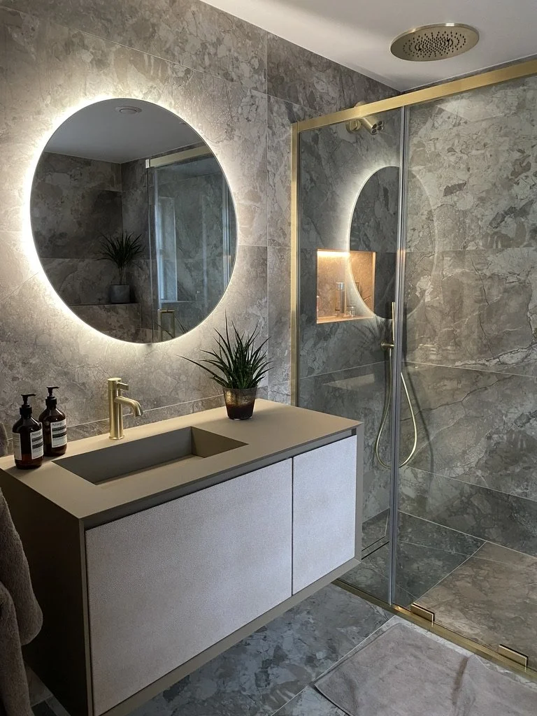 large format tile. Wall hung vanity and basin. Large round illuminated mirror. Walk in shower with brass and glass shower screen