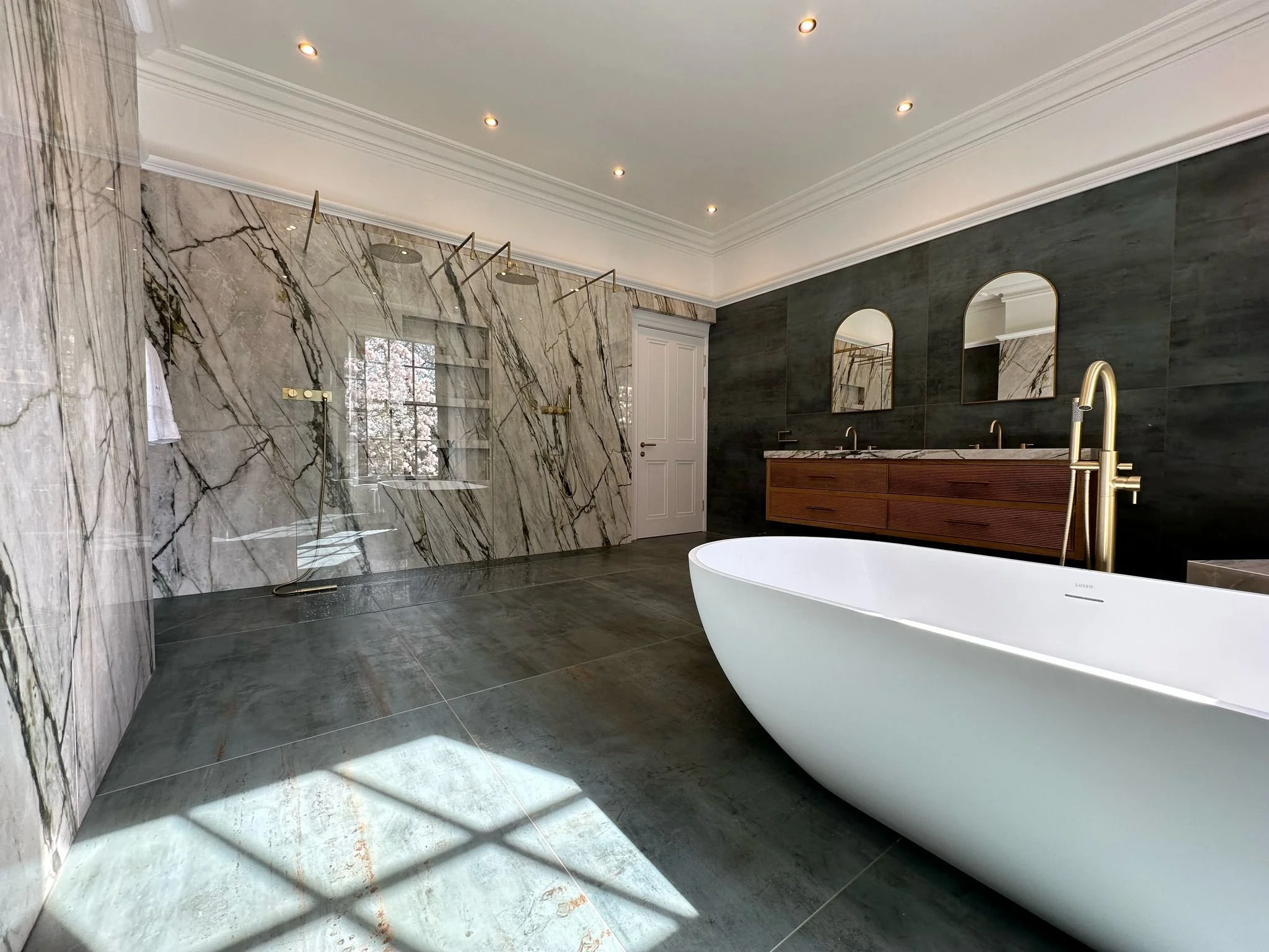Large family bathroom. Double shower. Large format tiles. Recessed shelves. Mitred edges. Double vanity. Bespoke double basins. Illuminated mirrors. Free standing bath. Floor mounted bath tap.