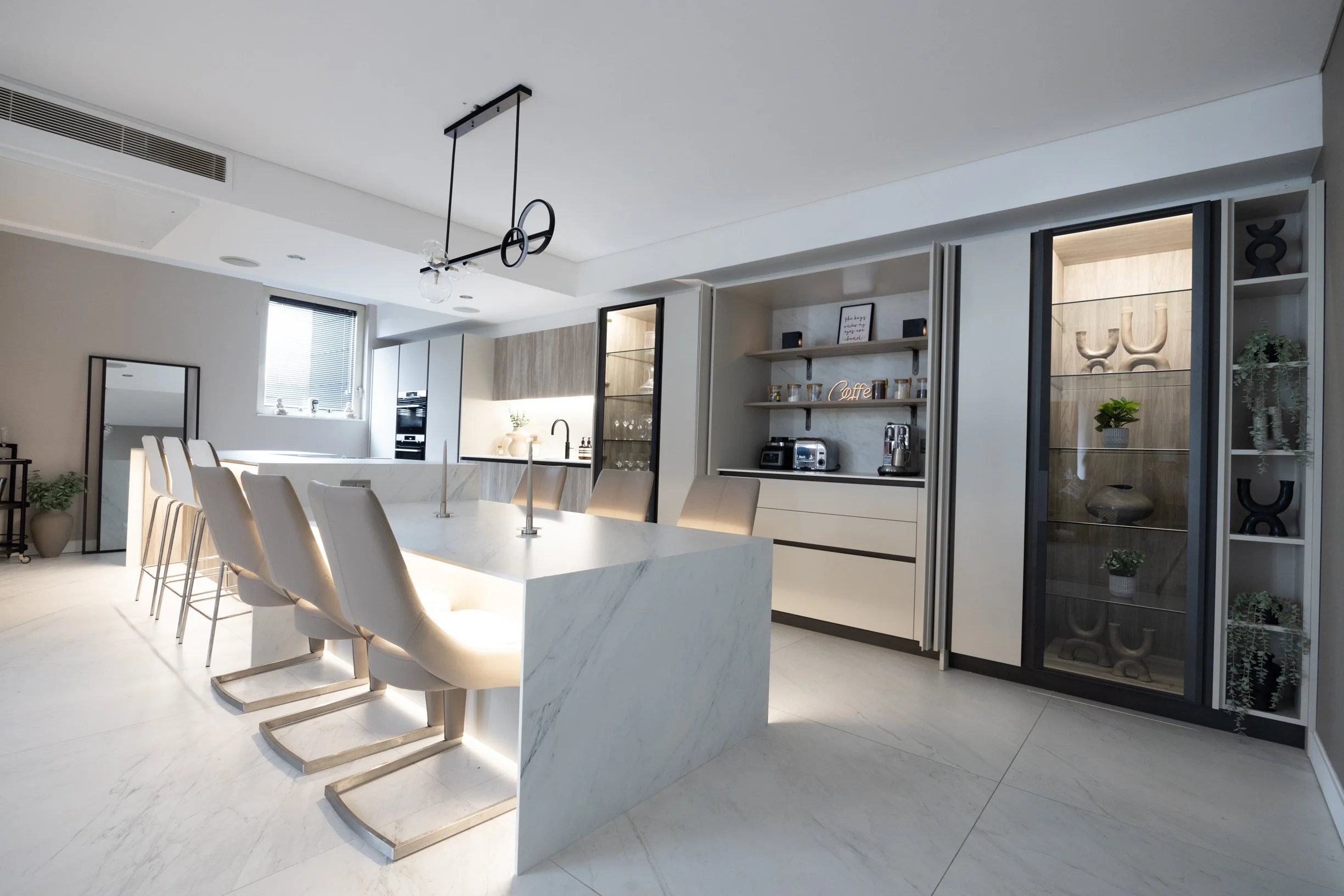 Penthouse apartment kitchen. Oversized, split level kitchen island. Breakfast station with pocket doors. LED lighting. TV wall. Bespoke, illuminated mirror. Large format floor tiles.