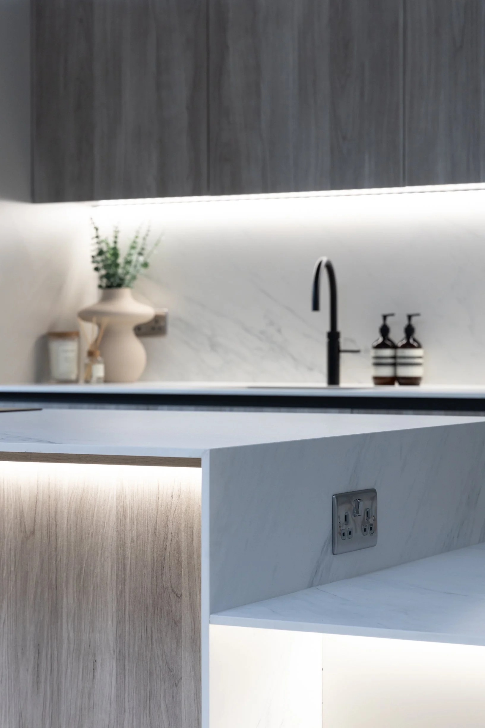 Penthouse apartment kitchen. Oversized, split level kitchen island. Breakfast station with pocket doors. LED lighting. TV wall. Bespoke, illuminated mirror. Large format floor tiles.