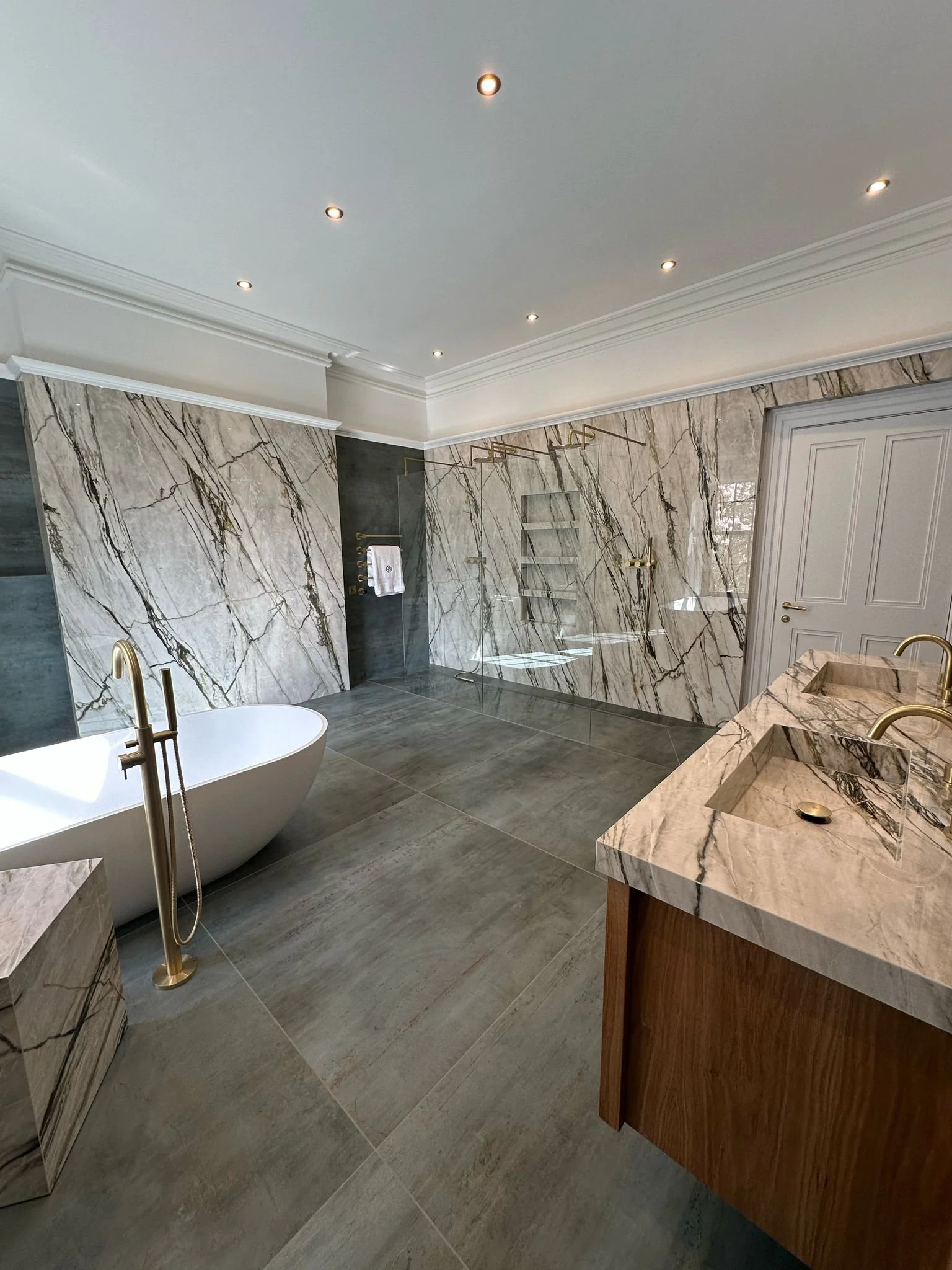 Large family bathroom. Double shower. Large format tiles. Recessed shelves. Mitred edges. Double vanity. Bespoke double basins. Illuminated mirrors. Free standing bath. Floor mounted bath tap.