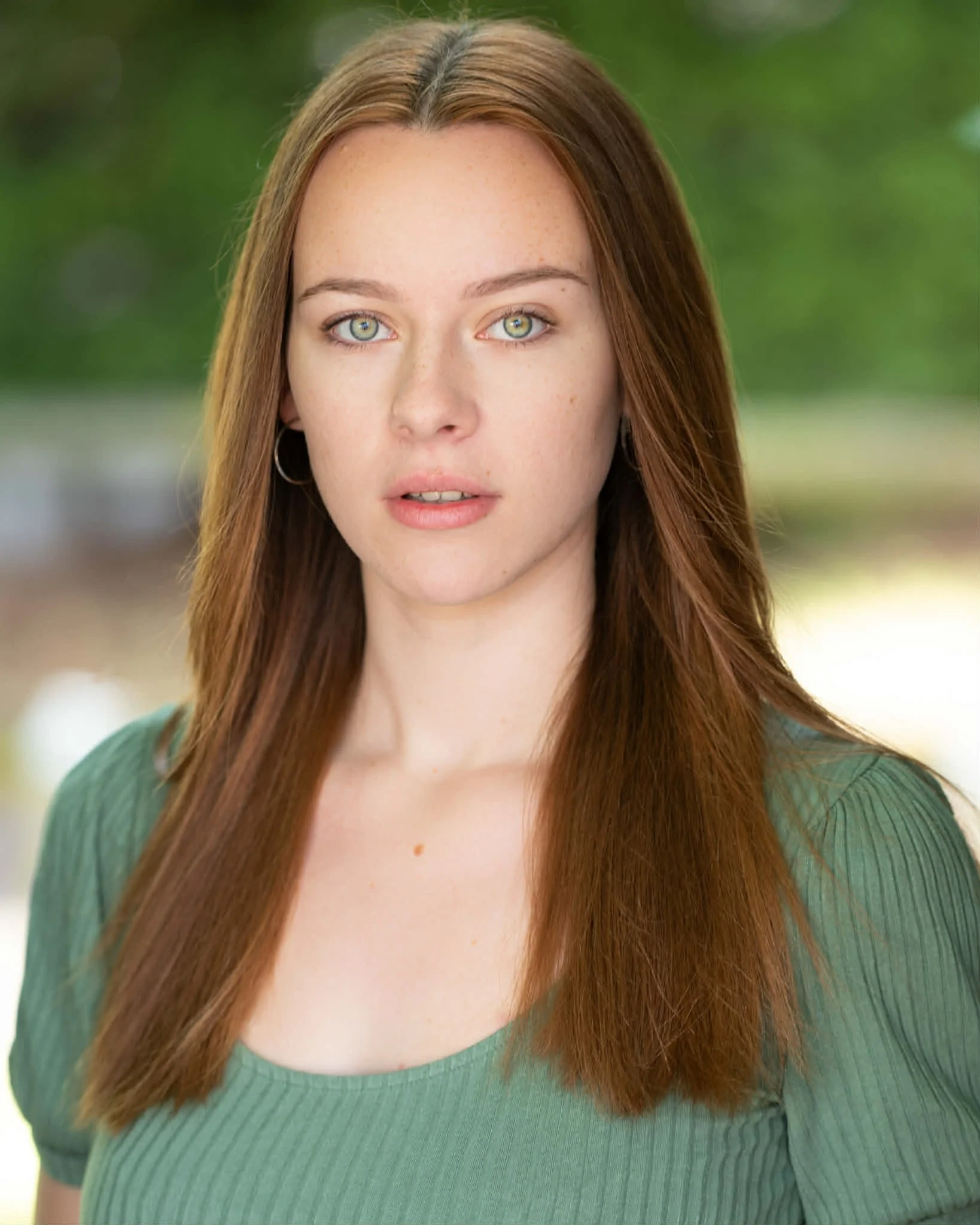A young woman with long red hair, blue eyes, and fair skin, smiling and wearing a black zip-up jacket, standing against a plain white background.