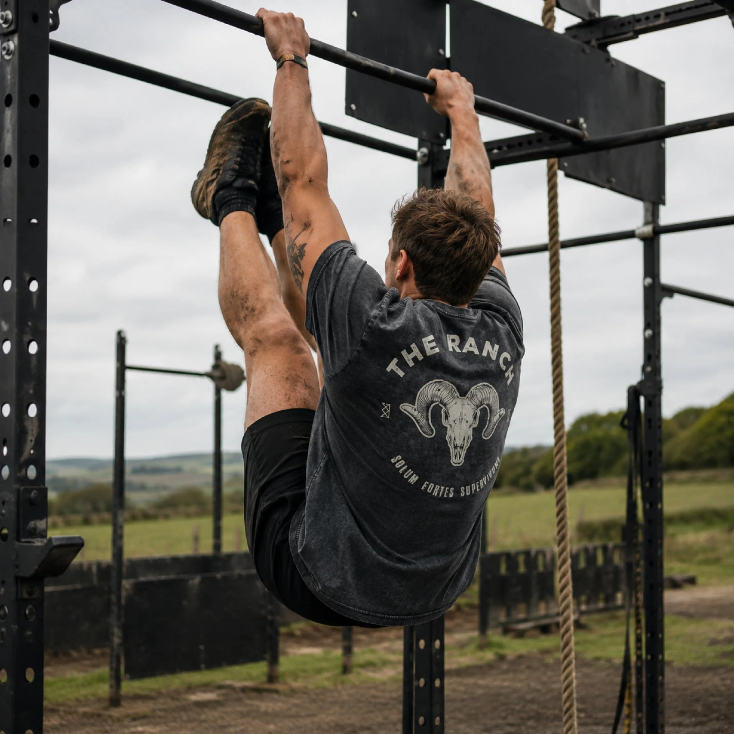 A man hanging from a pull-up bar with outdoor gym equipment and cloudy sky in the background.