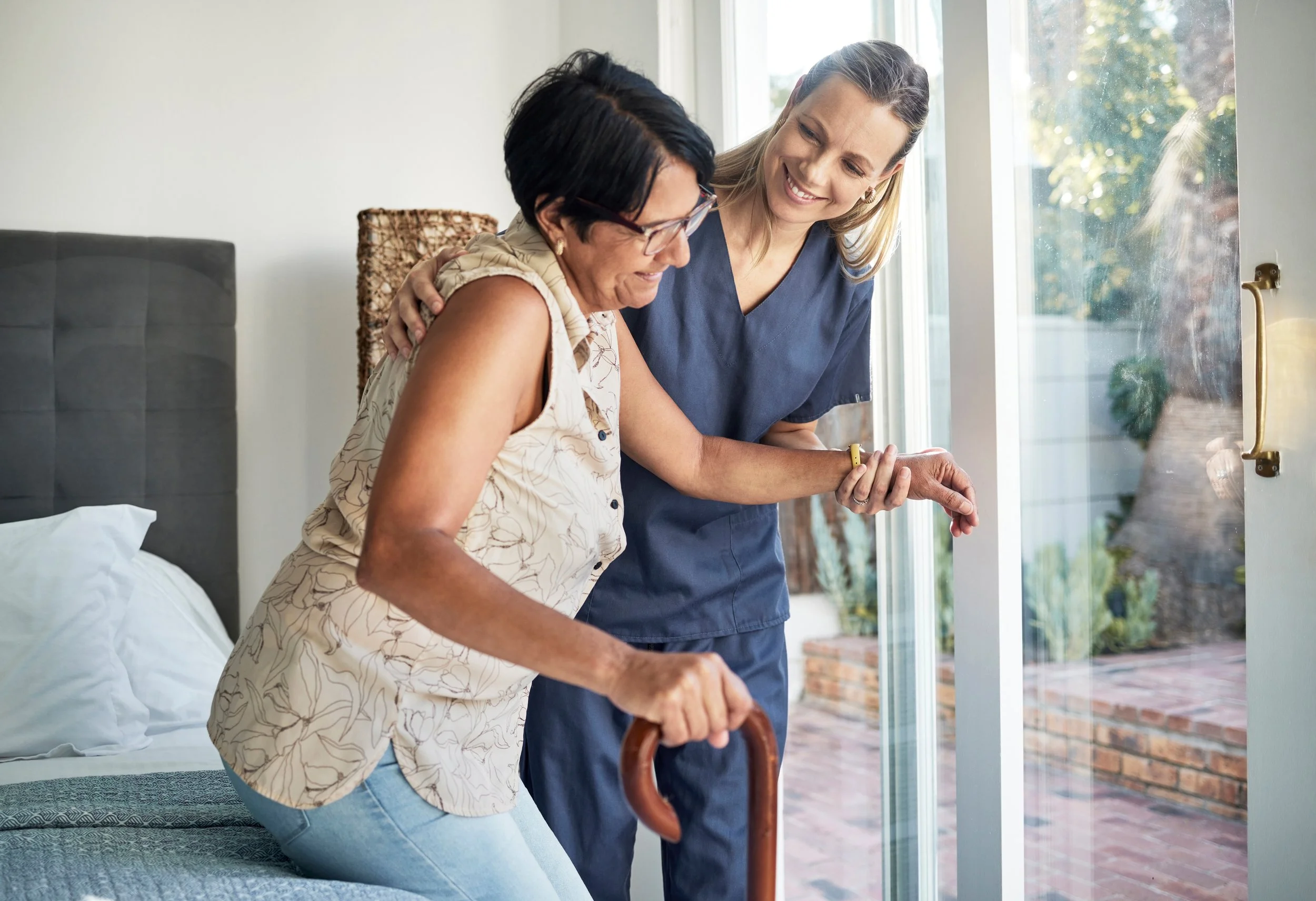 Caregiver assisting elderly woman with cane in bright room