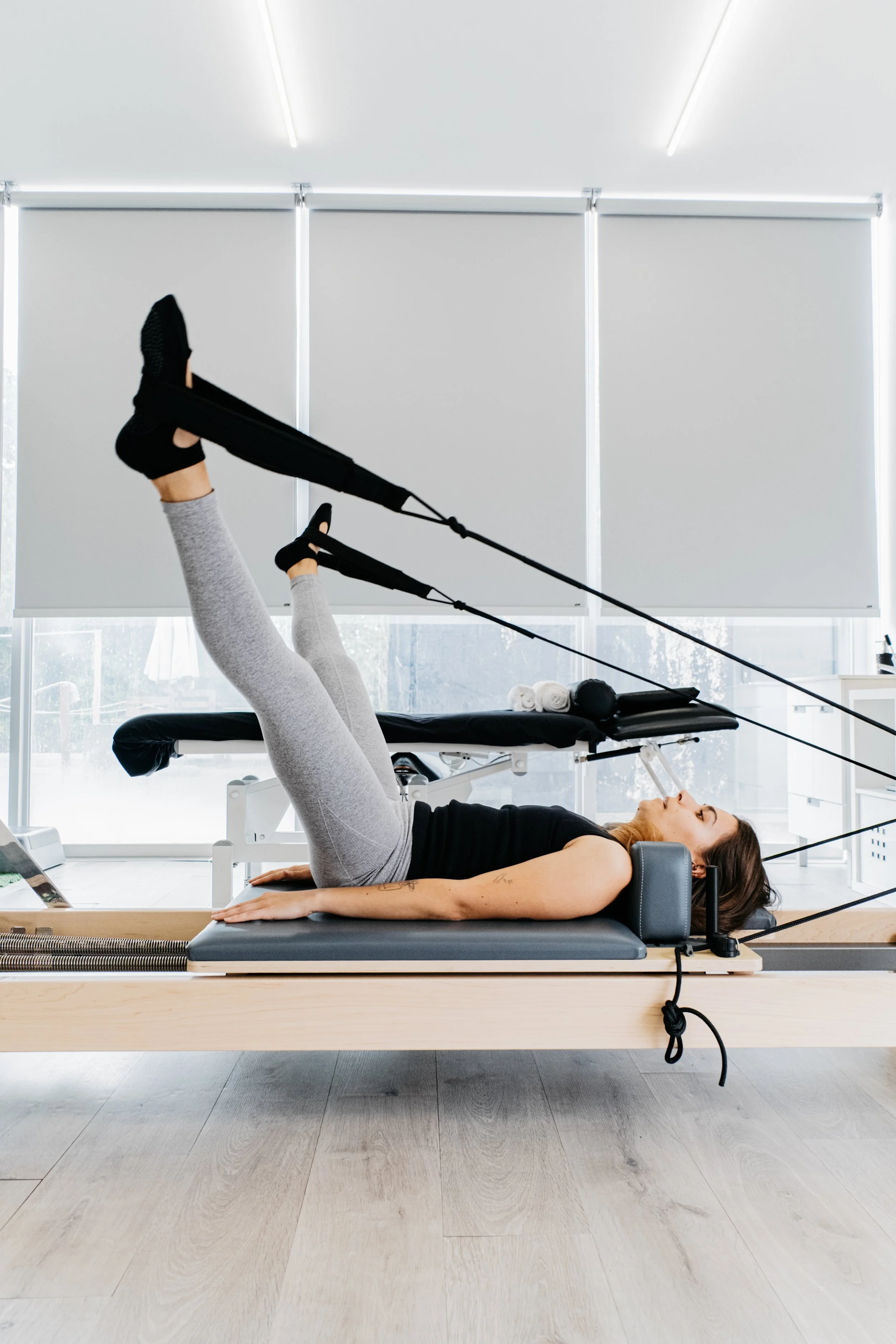 Pessoa realizando exercício de pilates deitada em uma cama de pilates com cabos de resistência.