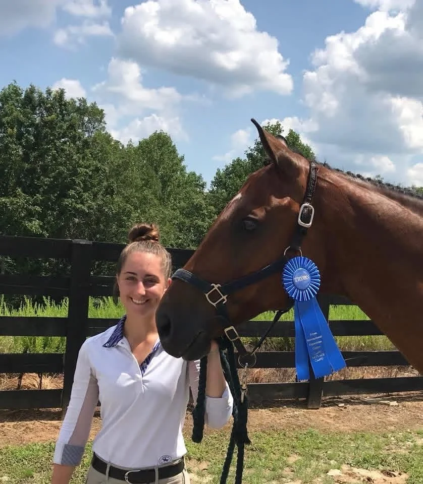 Woman smiling while standing next to a brown horse on a farm at Peace of Mind Equestrian Academy.