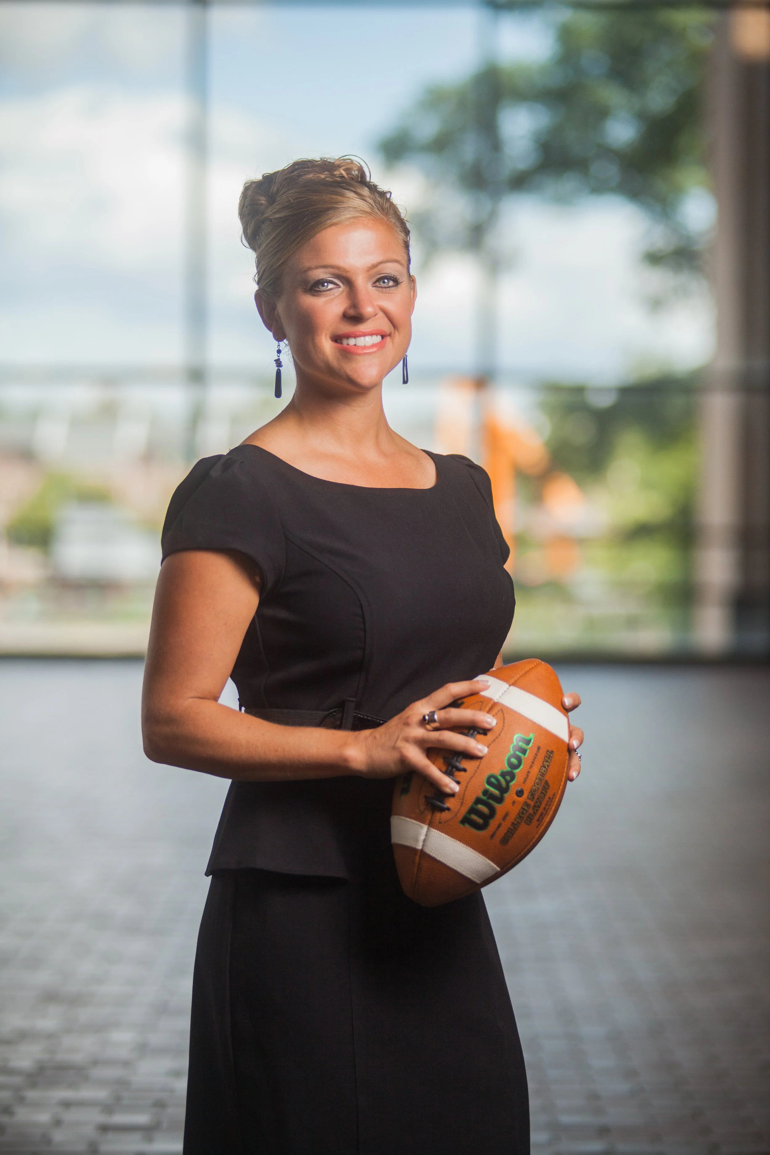 Woman in a black dress holding a football indoors.
