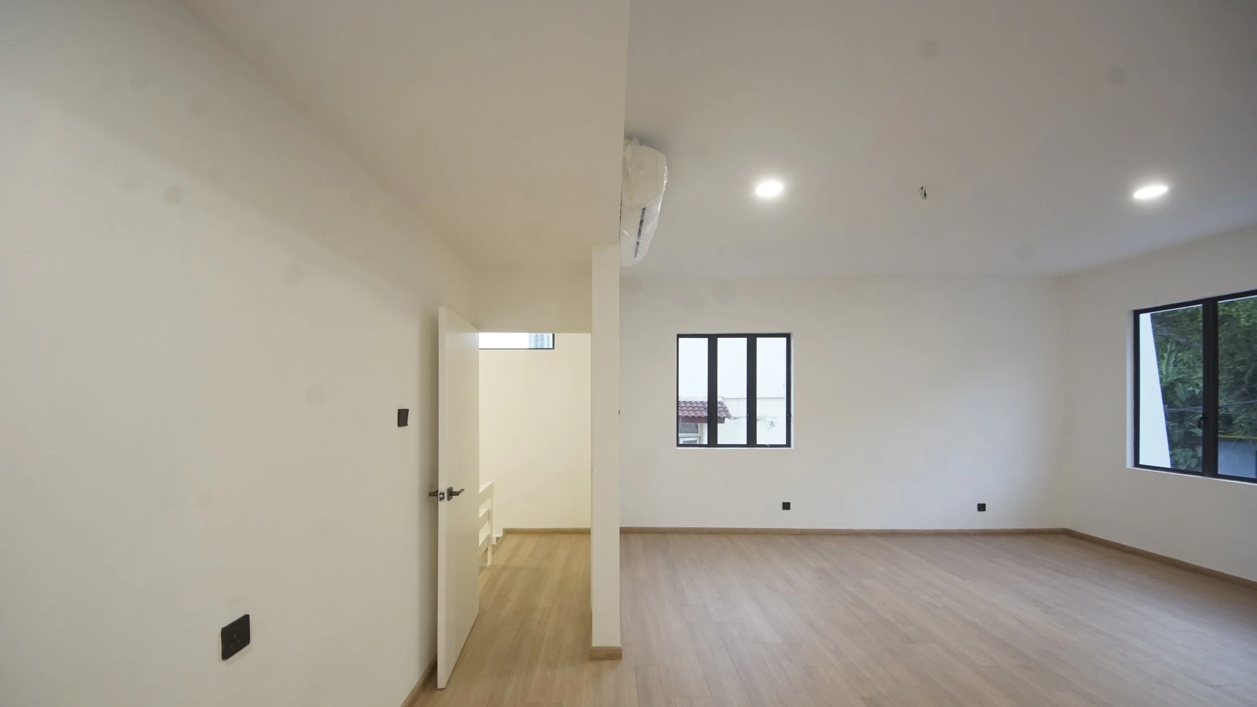 Empty room with light wood flooring, white walls, a partially open door, and windows.