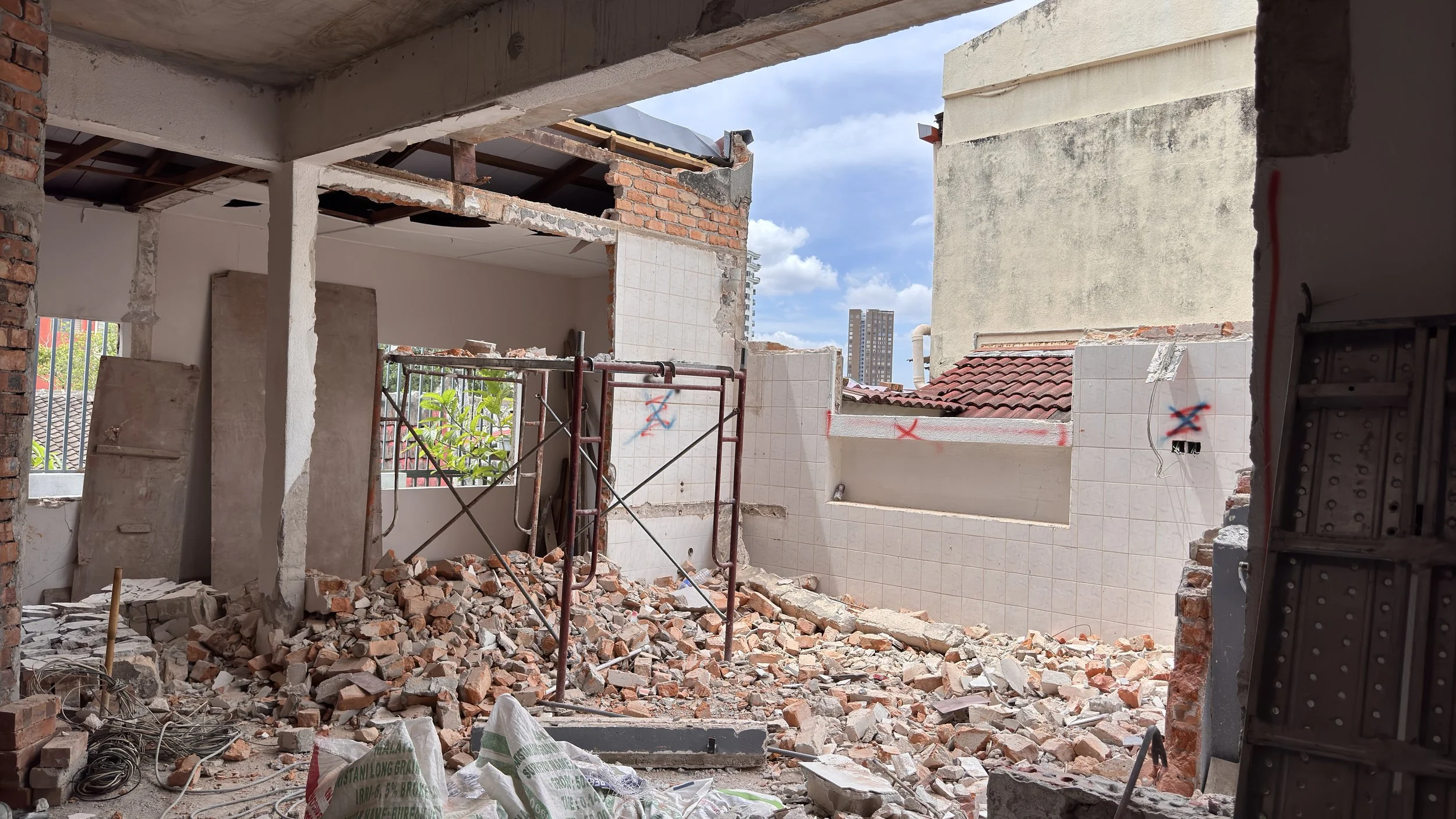 Renovation site with demolished interior walls, exposed brick, debris, and construction materials.