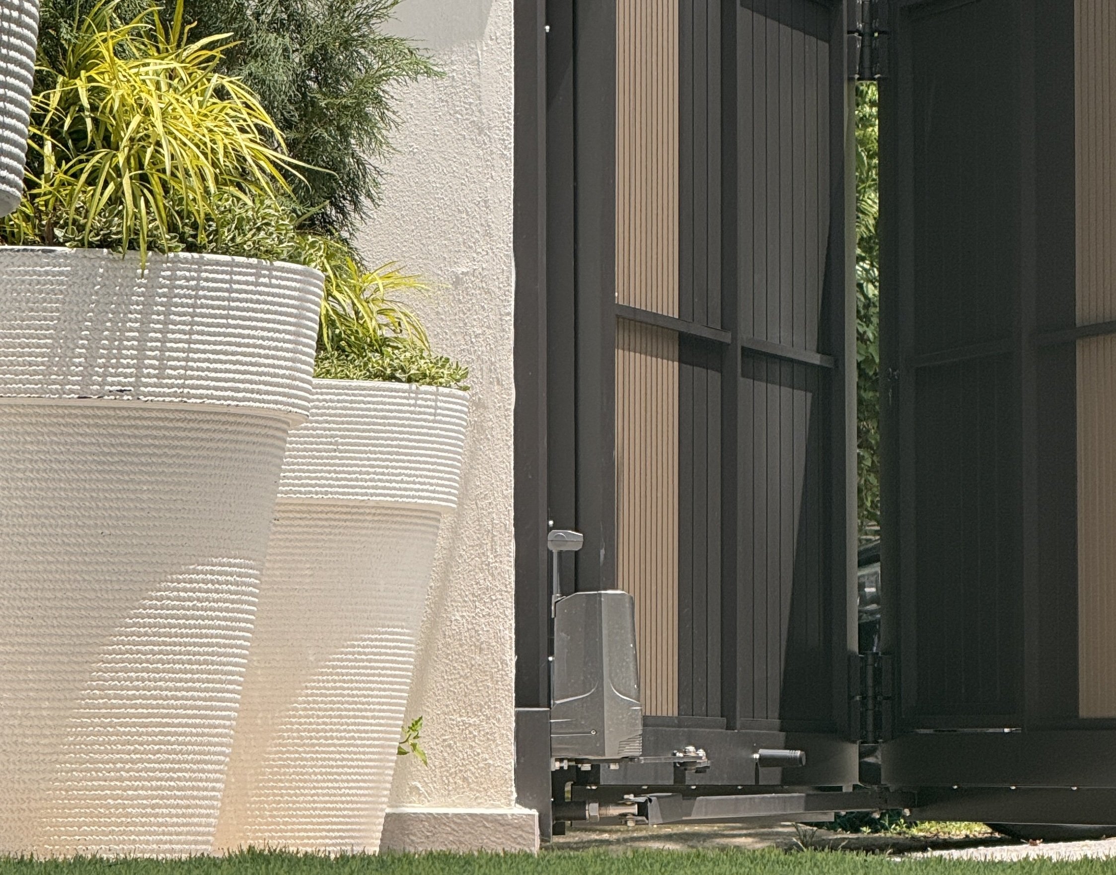 White textured planters with greenery beside a partly open black gate.