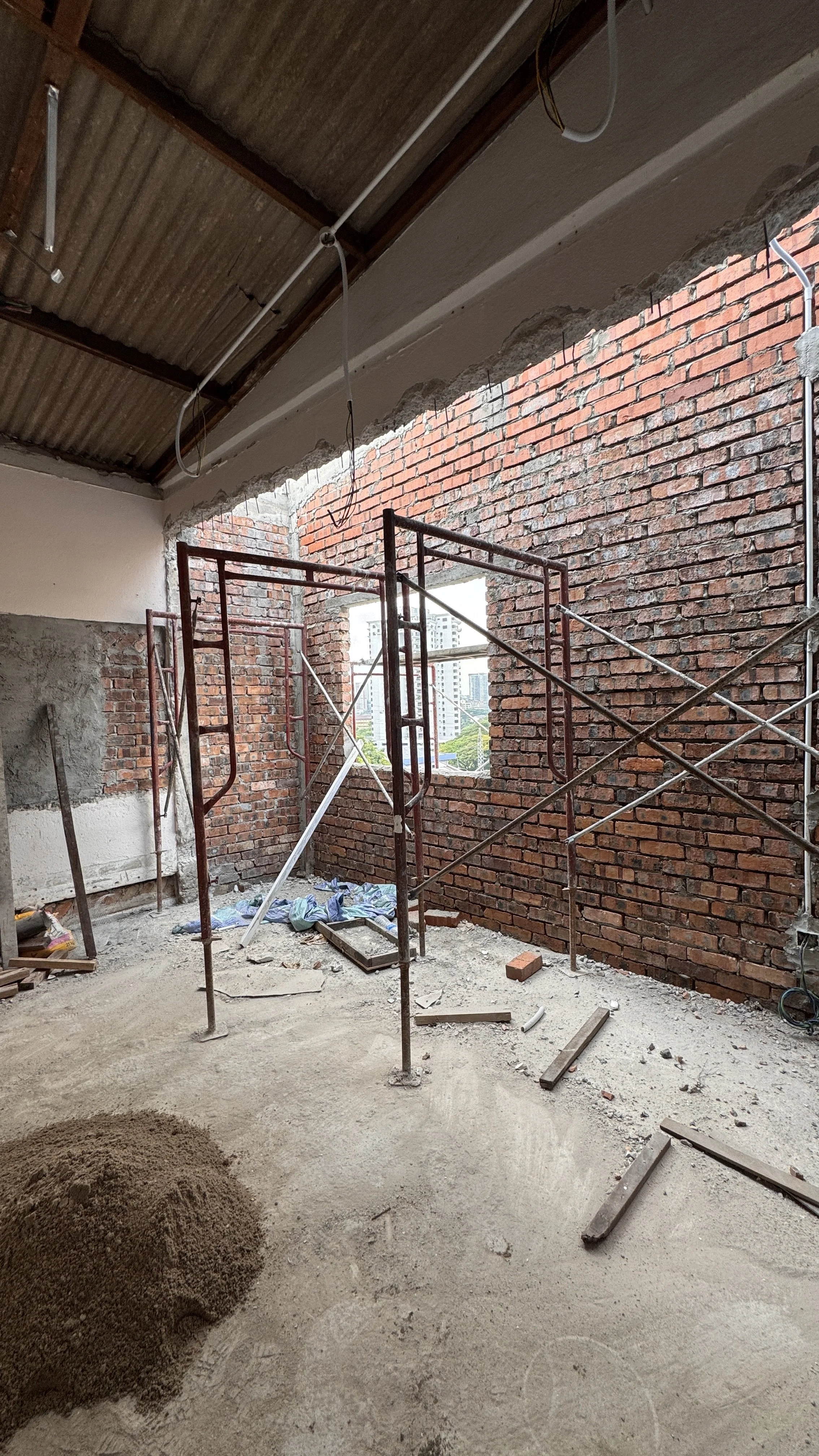 Construction site with brick walls and scaffolding, featuring unfinished windows and a pile of sand on the concrete floor.