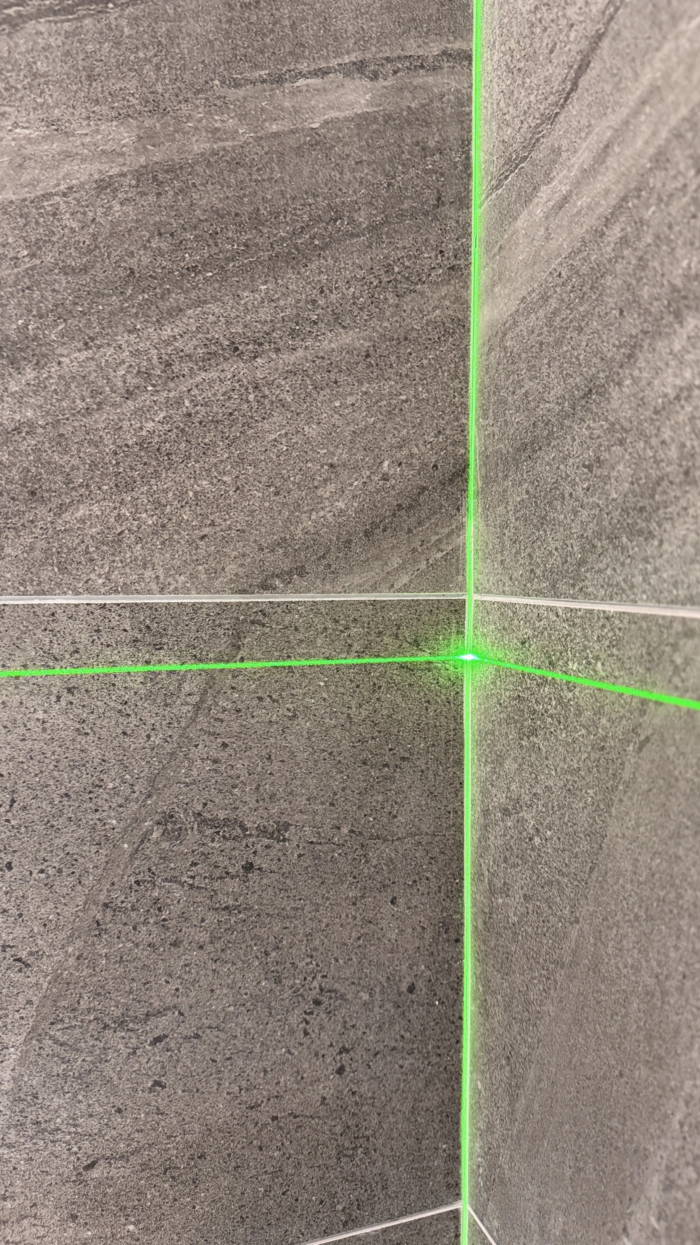 Gray tiled wall corner with intersecting green laser lines