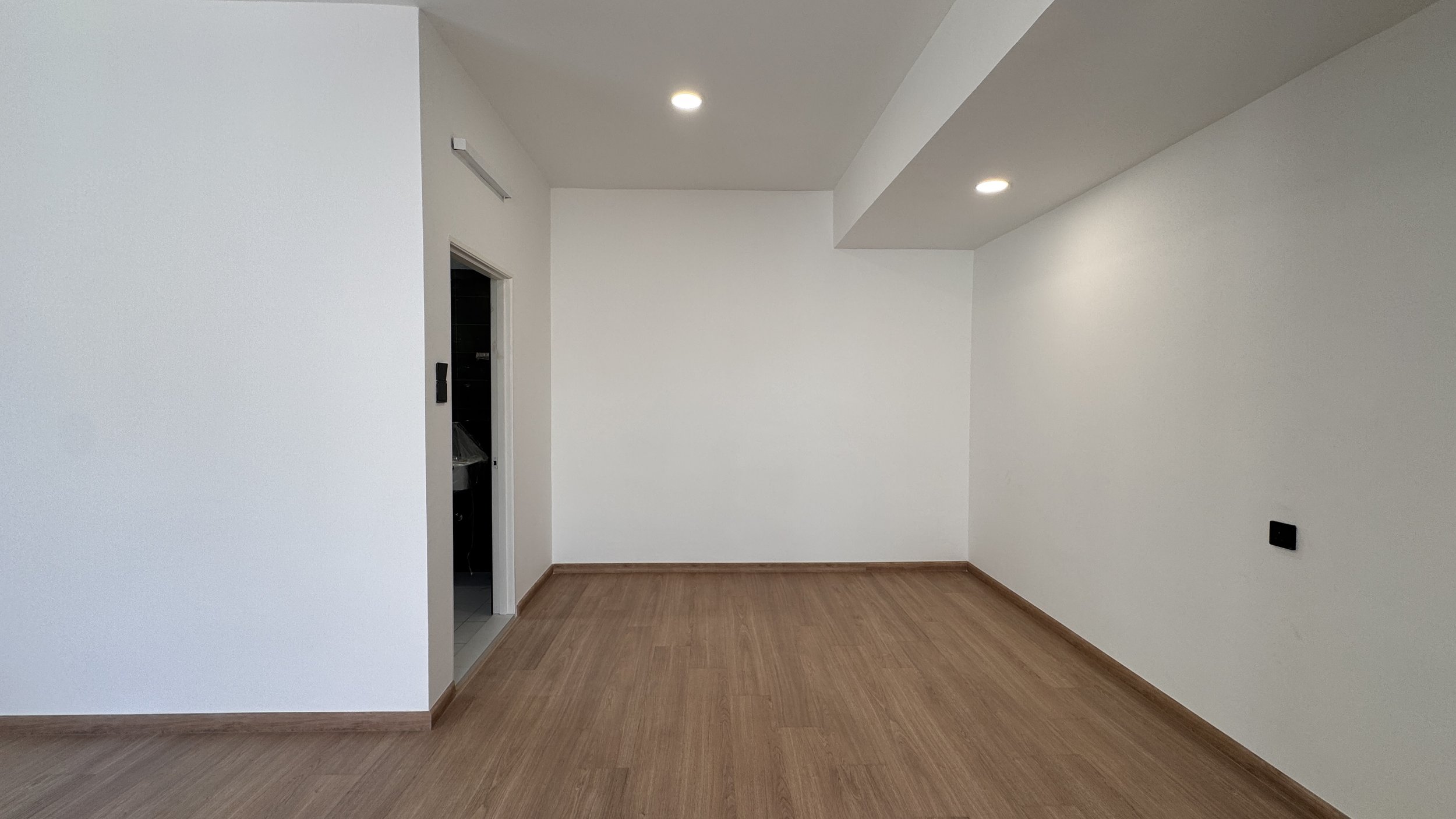 Empty room with white walls, wooden floor, and a small entrance to another room.