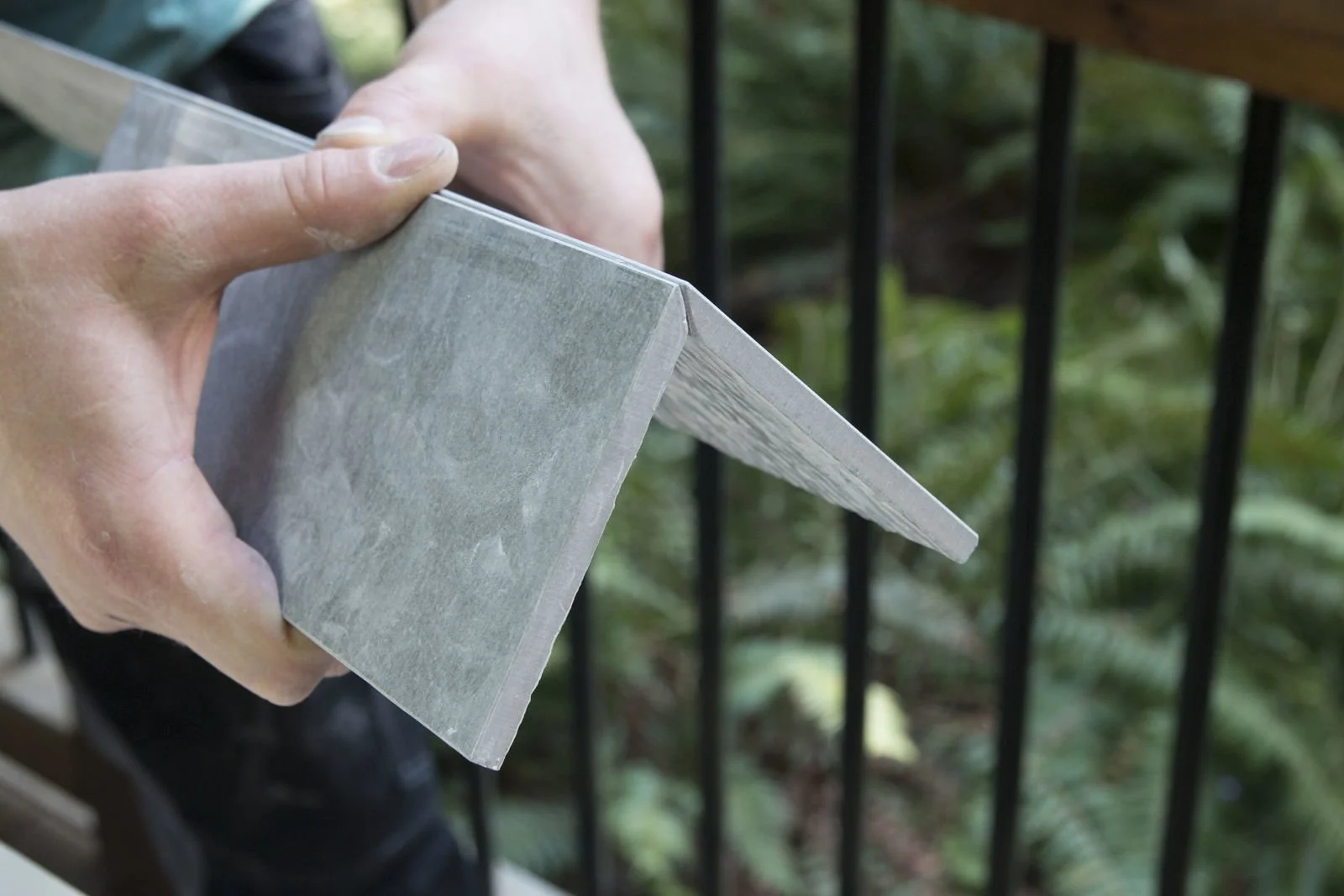 Person holding a piece of cement board near a railing.