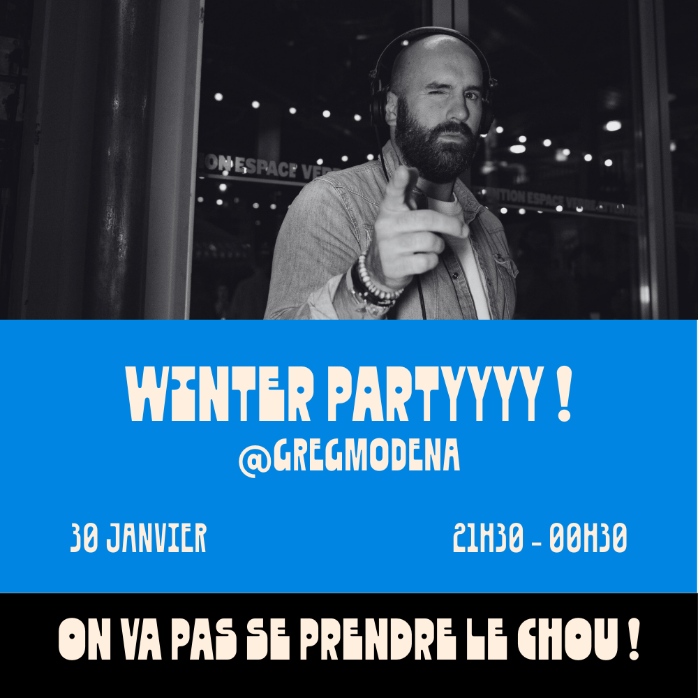 Un homme avec une barbe porte des écouteurs, fait un clin d'œil et pointe du doigt vers l'appareil photo. Il se trouve derrière une fenêtre ou un mur en verre, dans un environnement intérieur avec des lumières suspendues, et un panneau en arrière-plan.