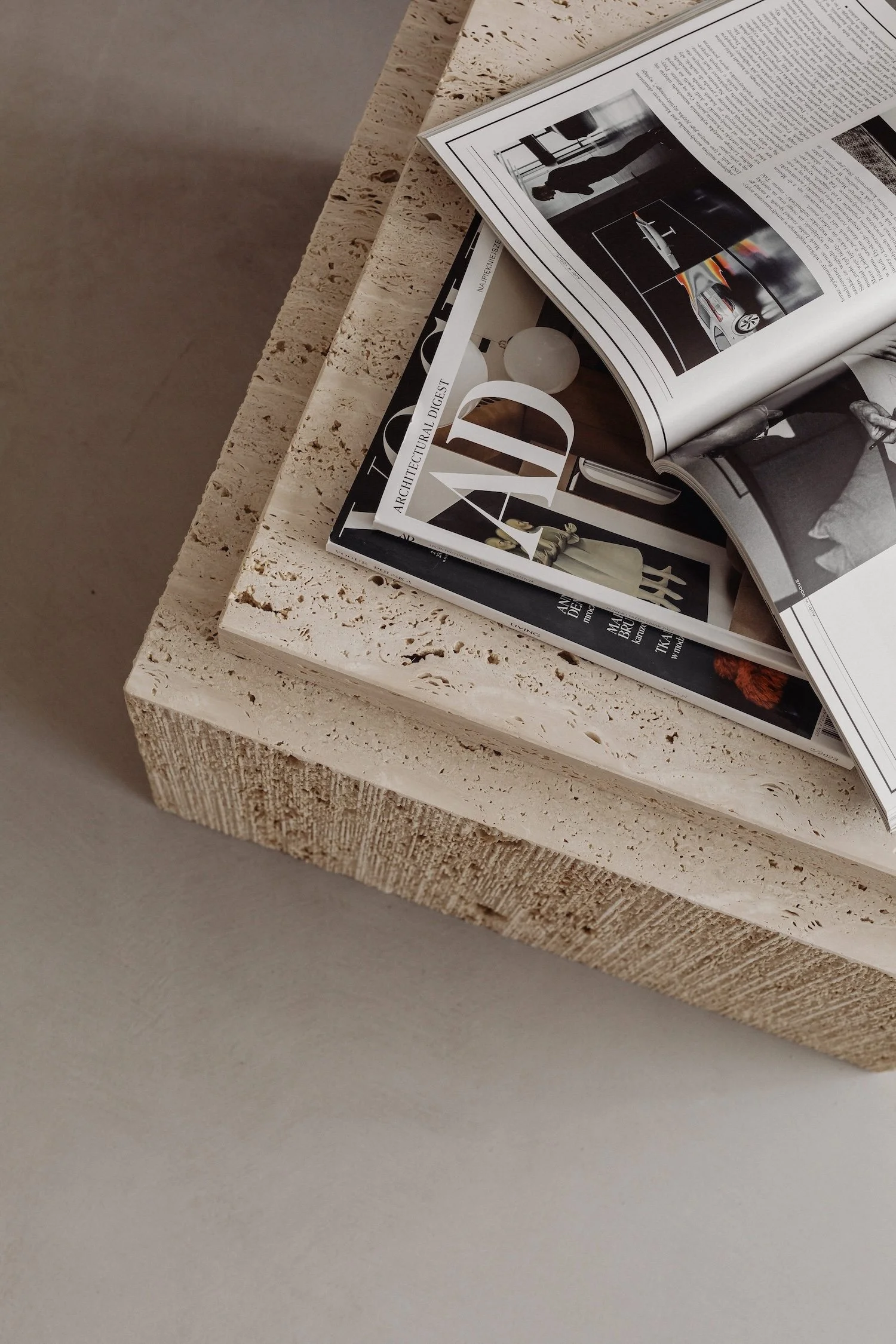 Stack of magazines on a rectangular, textured stone table with a neutral-colored surface.