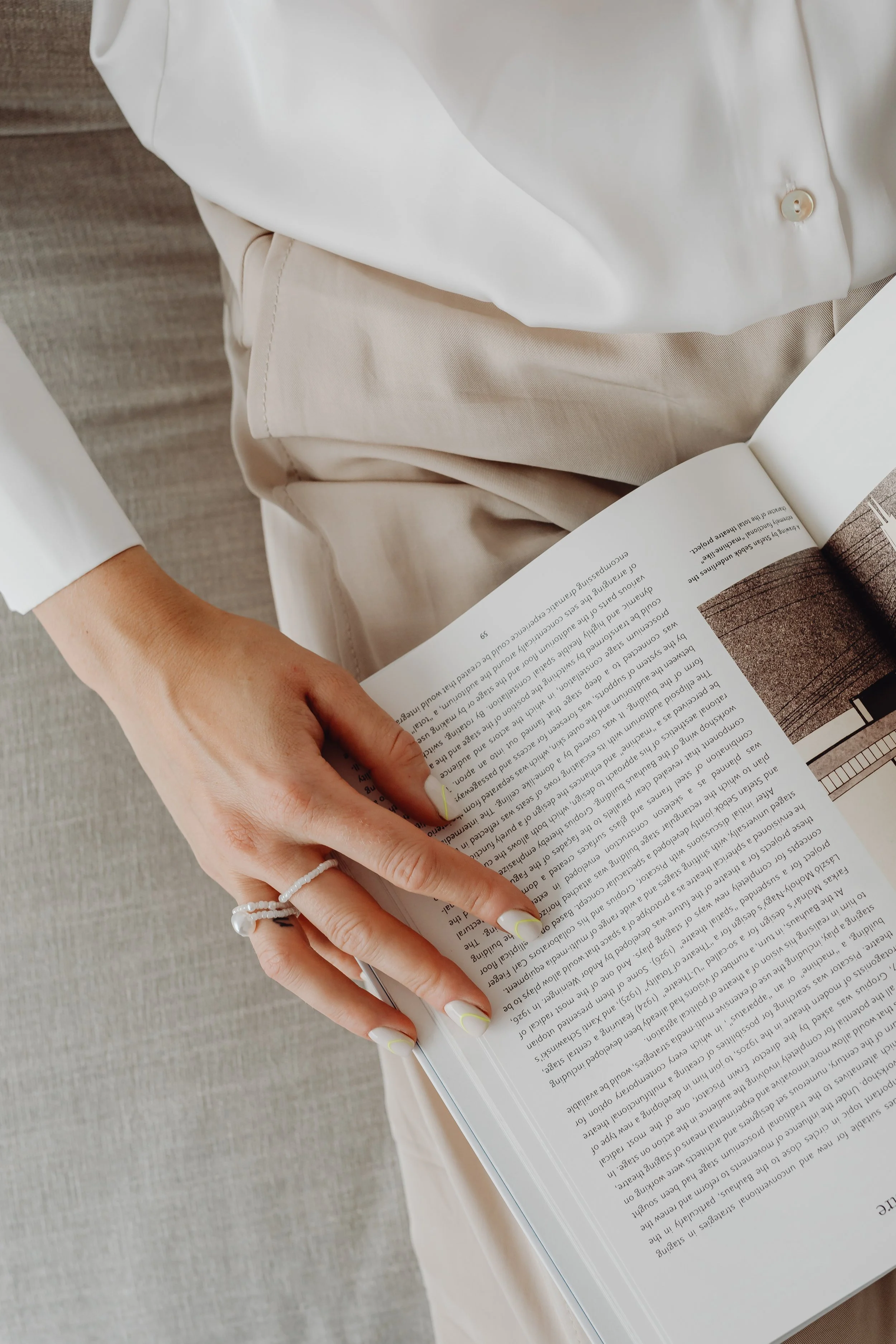 Person wearing white shirt and beige trousers sitting and holding an open magazine.