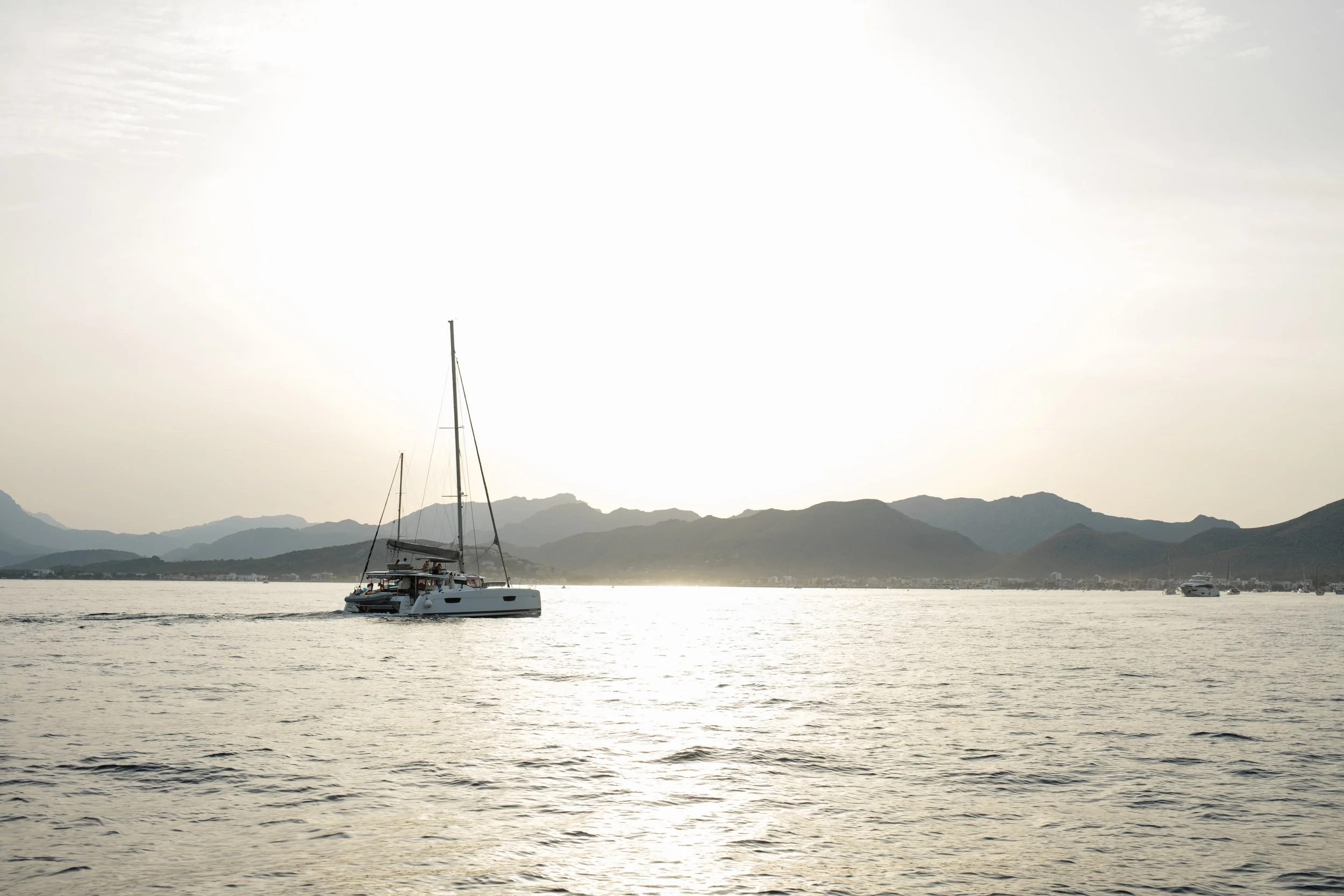 A sailboat on calm water with distant mountains and a partly cloudy sky in the background.