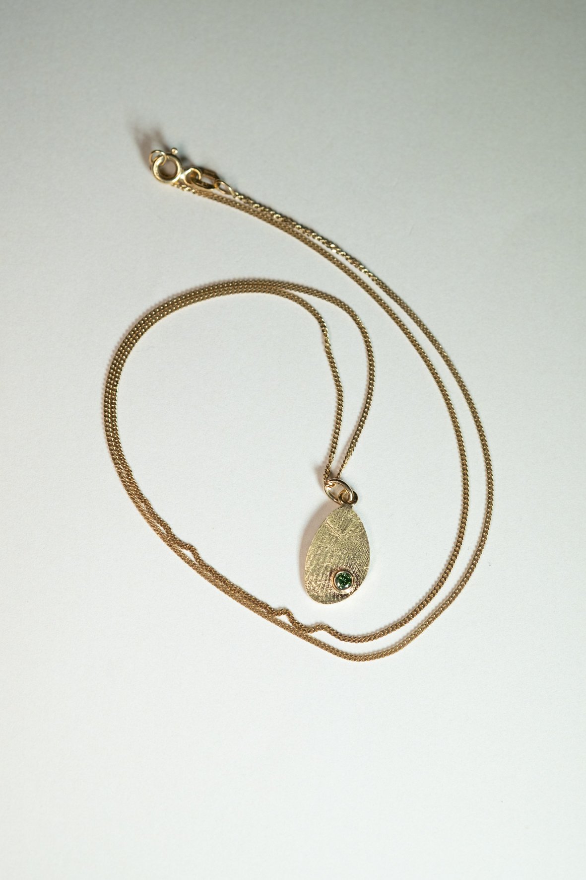 Gouden ketting met een hanger met een groene steen.