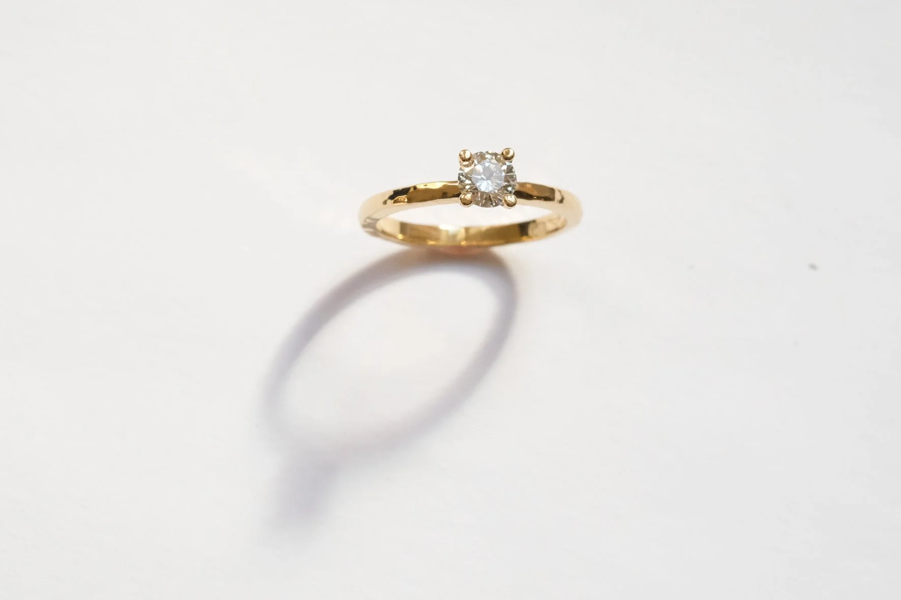 Gouden ring met een enkele diamanten edelsteen op een witte achtergrond, met een schaduw onder de ring.