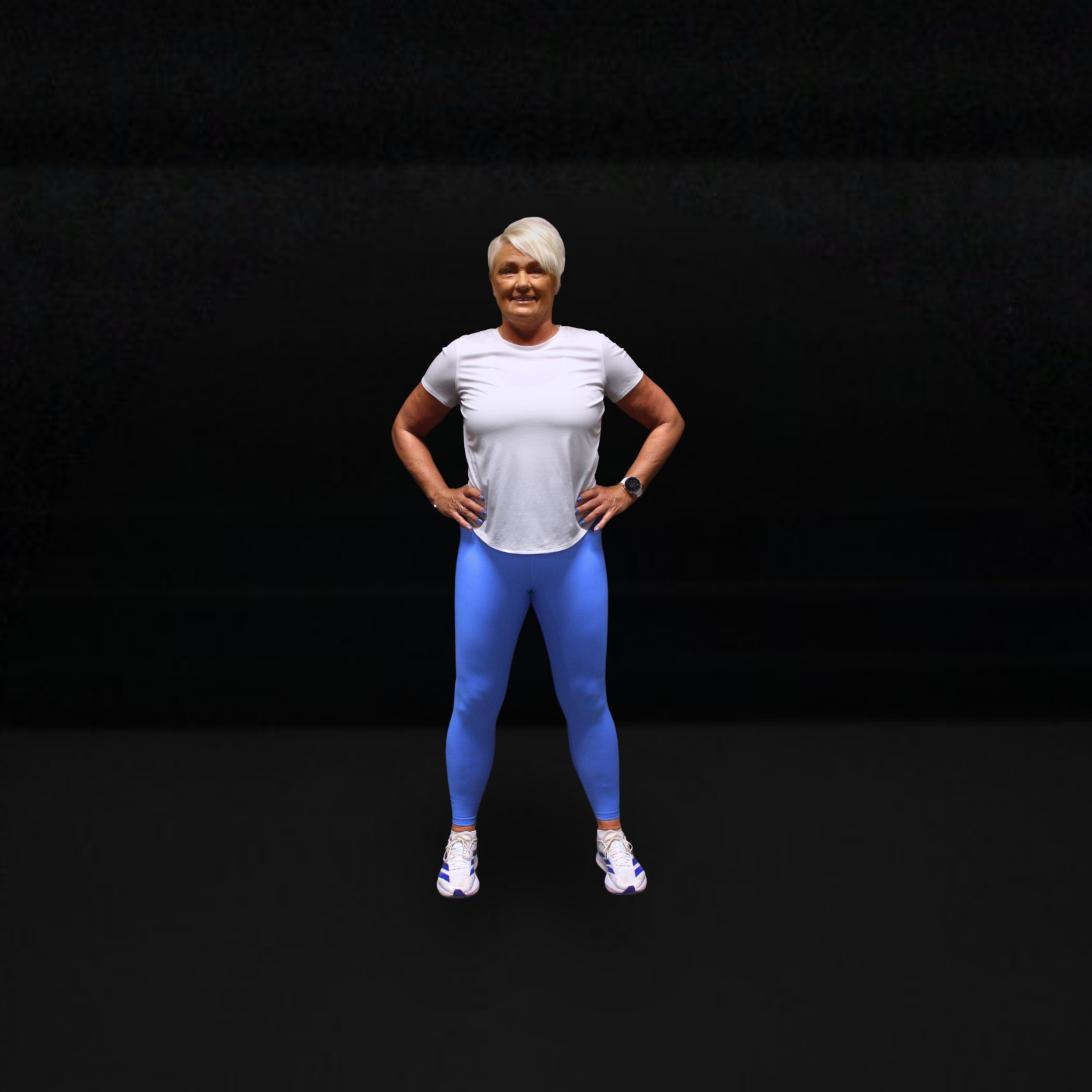 Person i treningsklær med hvit t-skjorte og blå tights, står med hendene i siden mot en mørk bakgrunn.