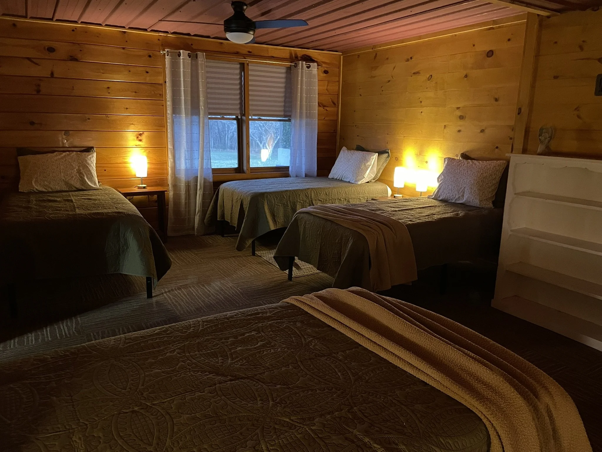 Cozy multi-bed room with warm lighting and rustic wood walls at Creekside Crafters women's retreat in Watertown, Tennessee