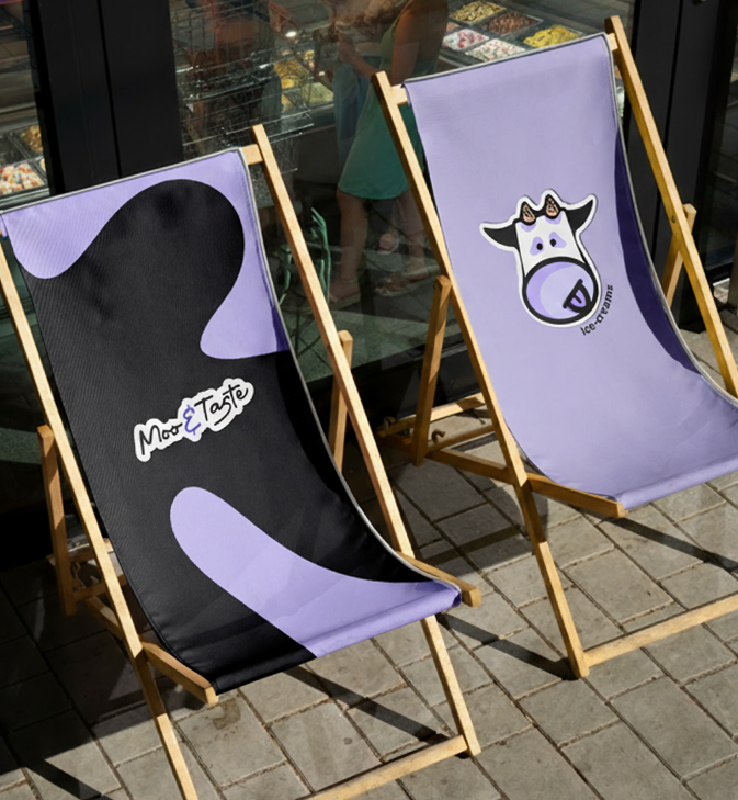 Two purple and black deck chairs outside a store with ice cream shop branding, one with a cow logo and the other with the words 'Most & Taste'.