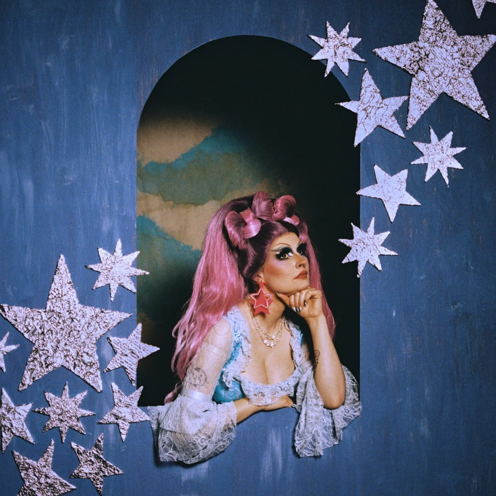 Neon Rodeo lead singer Amber Sands in a pink wig, posing in a blue arch decorated with silver stars