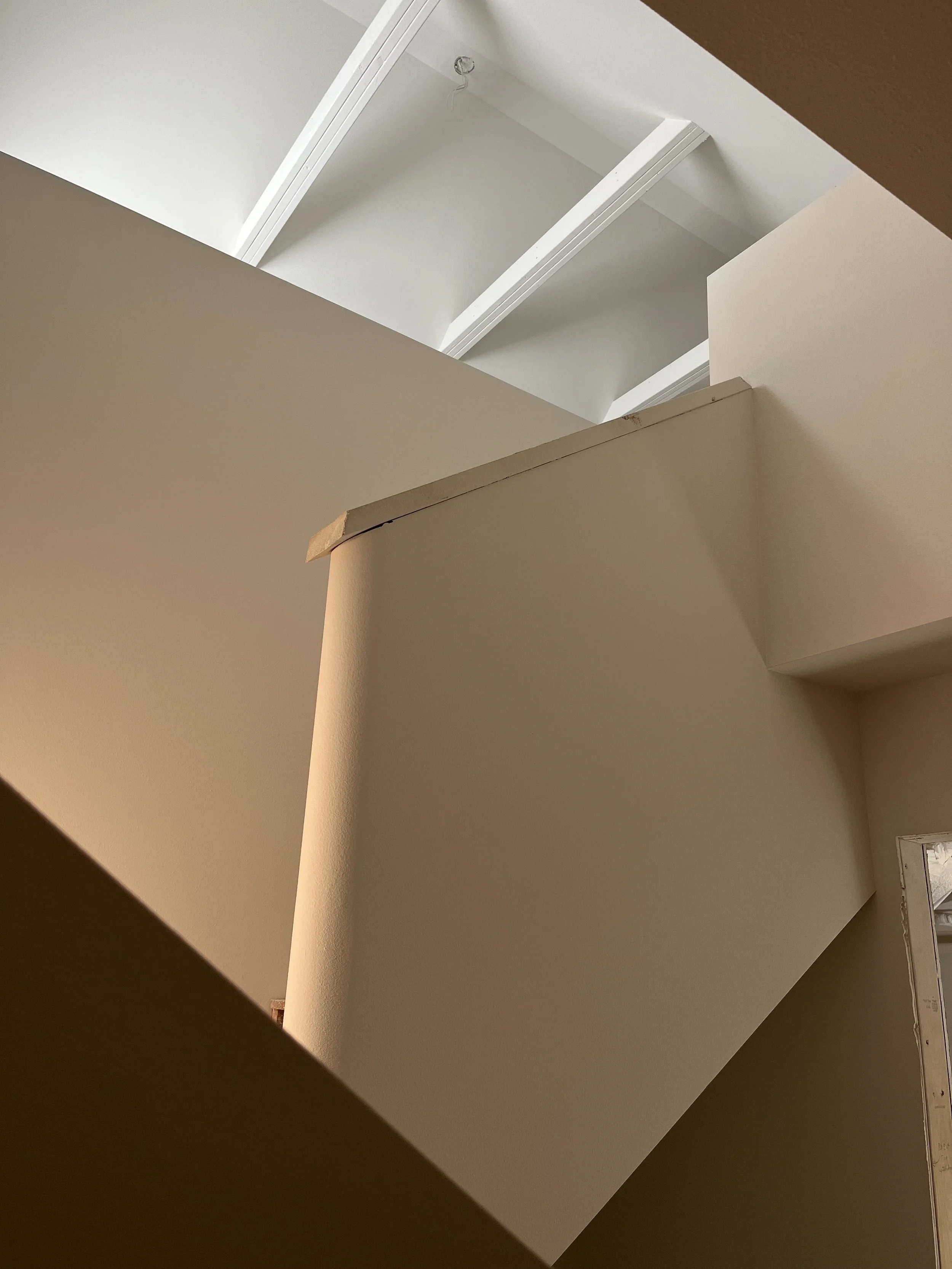 Interior of a building under construction showing ceiling beams, walls, and part of a stairwell or opening.